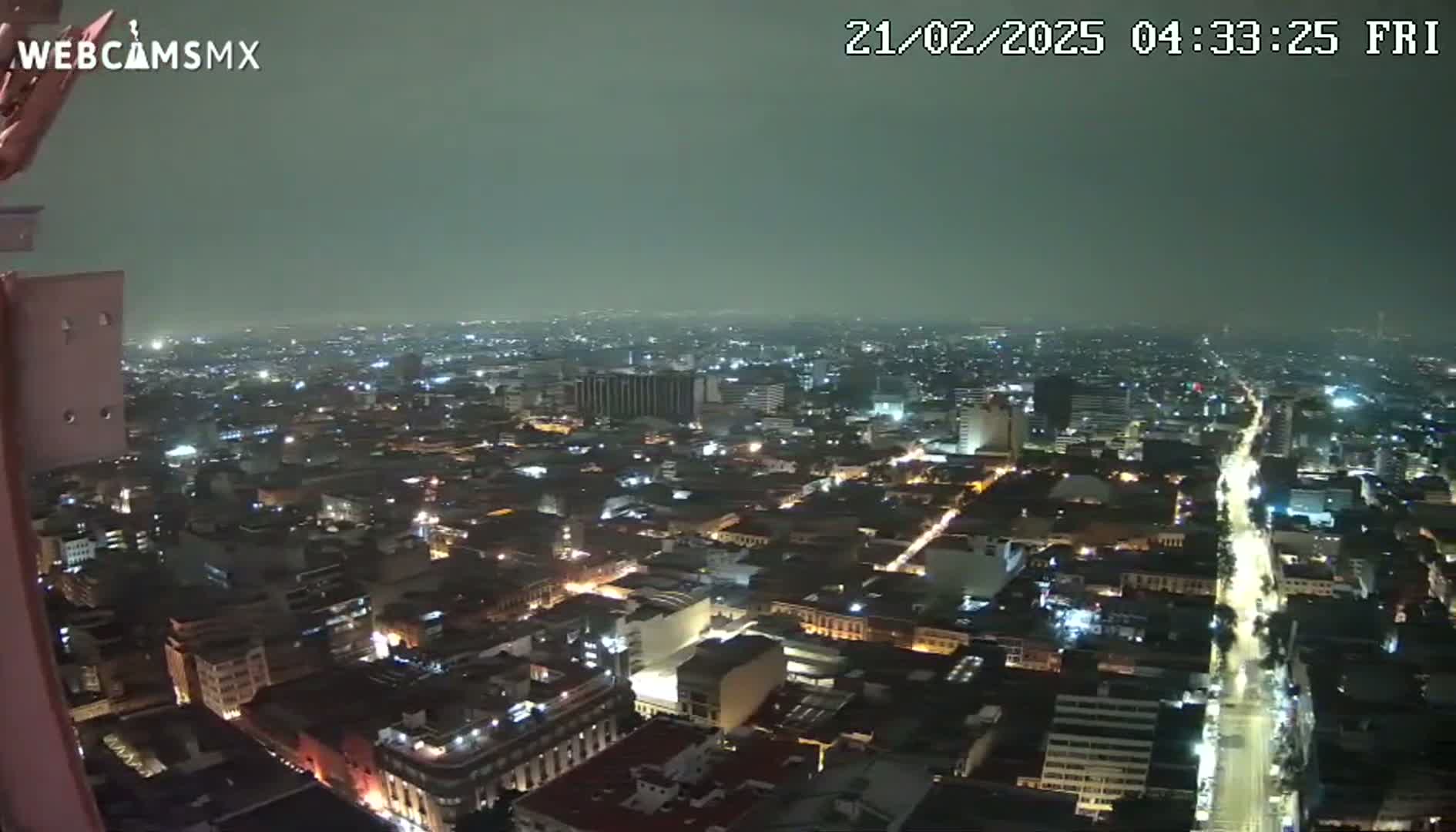 A nighttime, high-angle view of a city with dimly lit streets and buildings under a hazy sky.