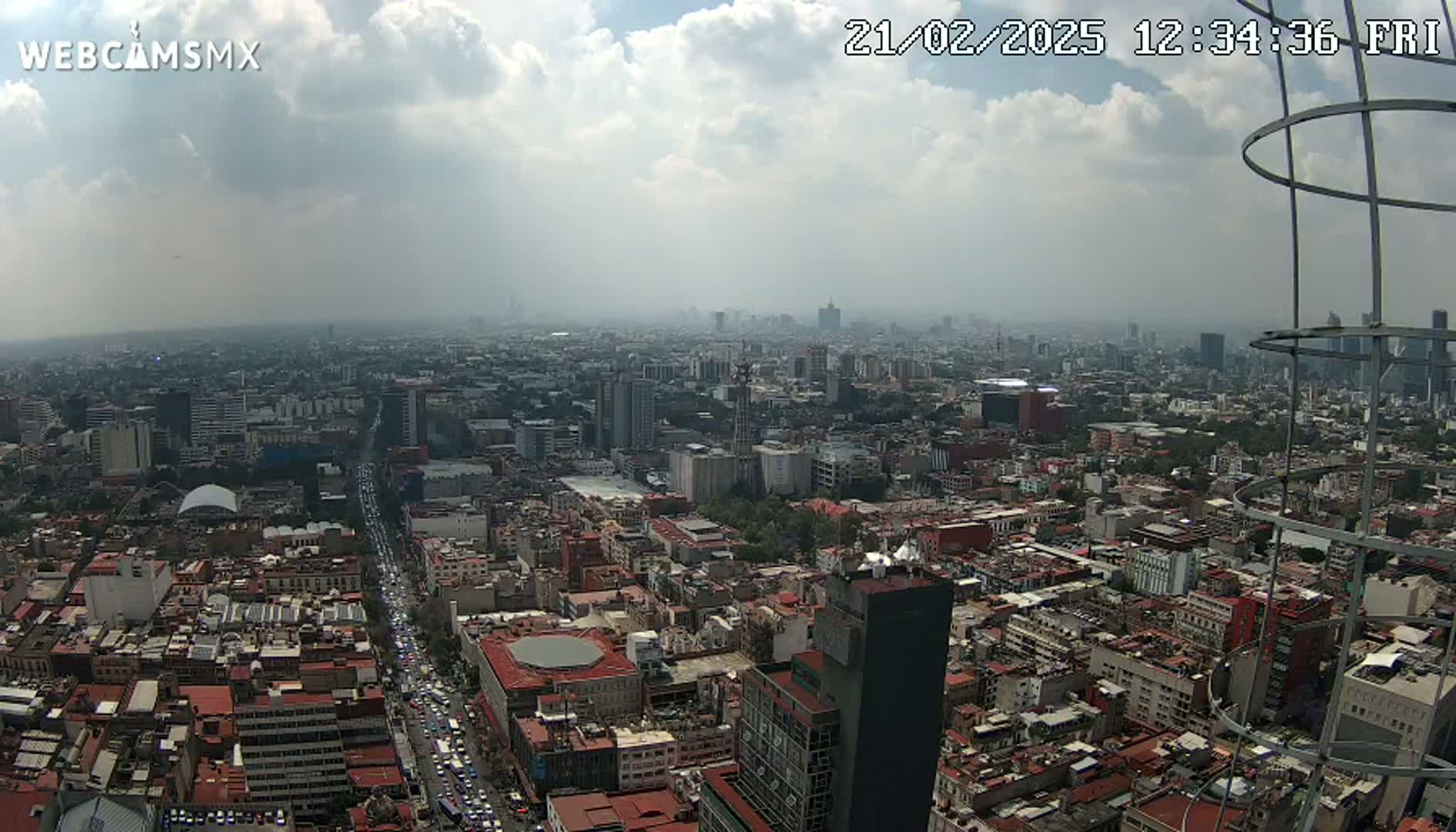 A hazy, partly cloudy day reveals a sprawling cityscape with many buildings, roads, and a metal structure in the foreground.