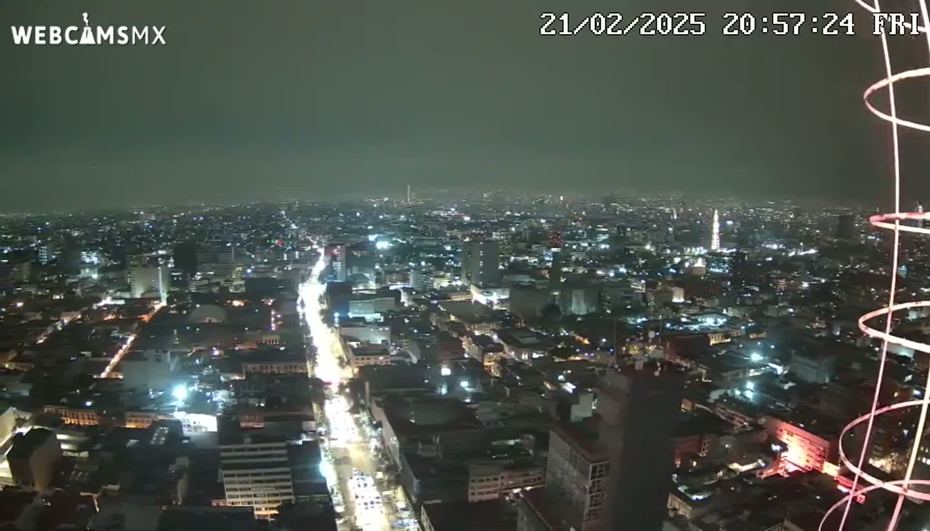 A nighttime aerial view of a city with a brightly lit street stretching into the distance under a clear, dark sky.