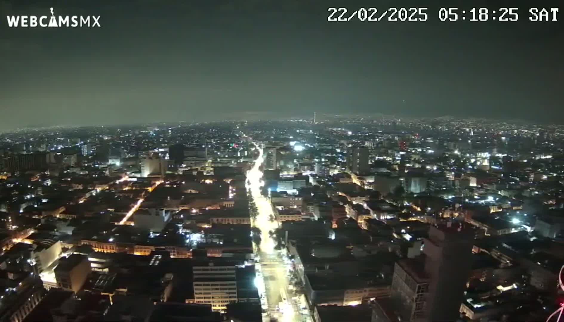 A nighttime, high-angle view shows a sprawling city illuminated by streetlights and building lights under a dark sky.