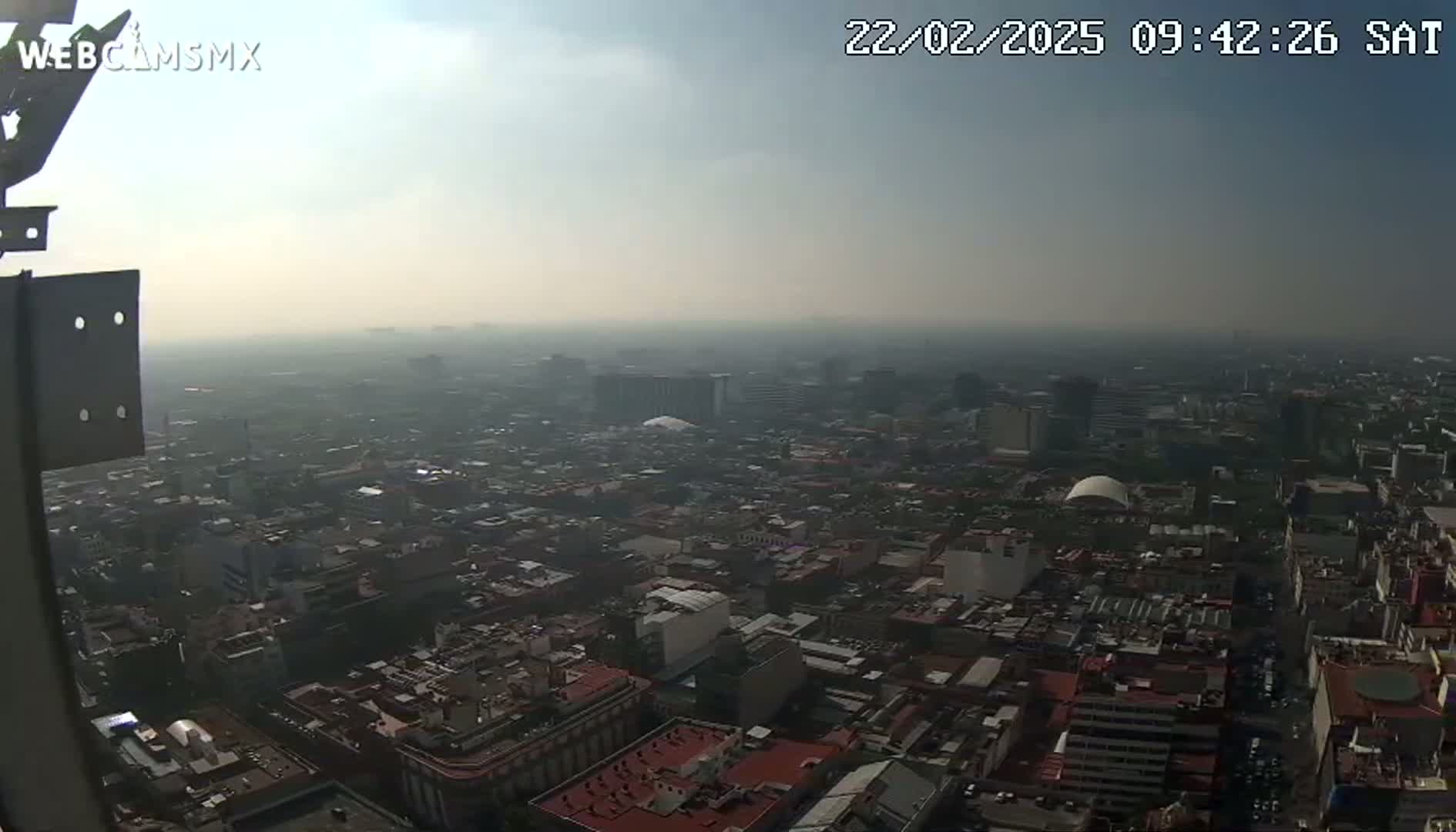 A hazy, high-angle view shows a sprawling city under a mostly clear sky.