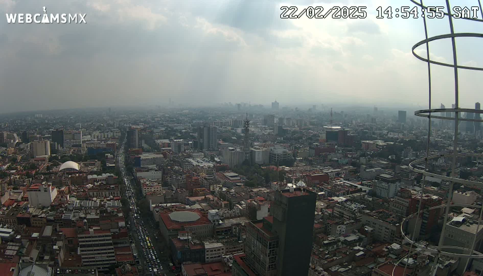 A hazy, overcast view of a sprawling city, seen from a high vantage point with a metal structure in the foreground.
