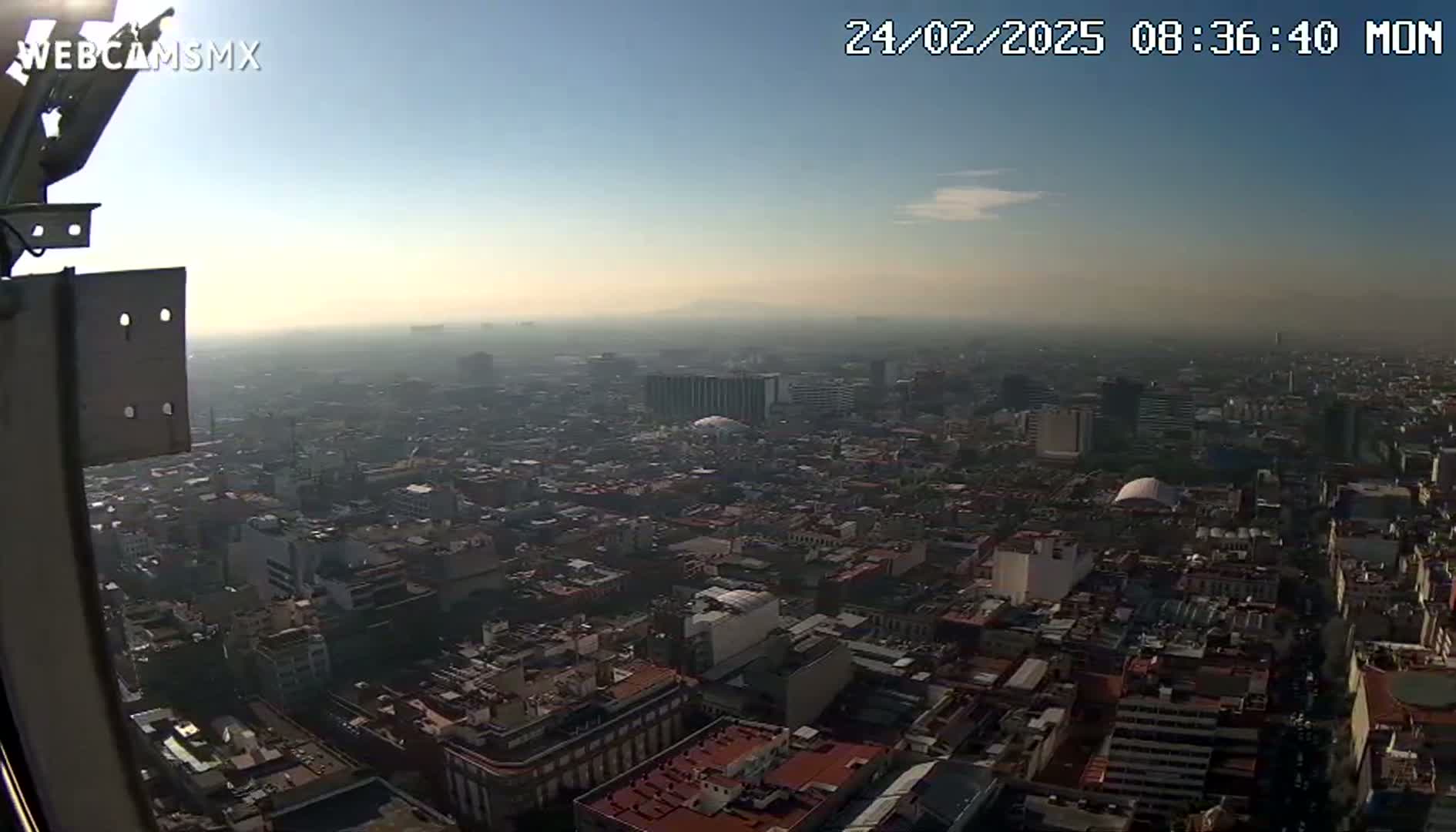 A hazy, sunny morning view from a high vantage point shows a sprawling city of densely packed buildings stretching to the horizon.