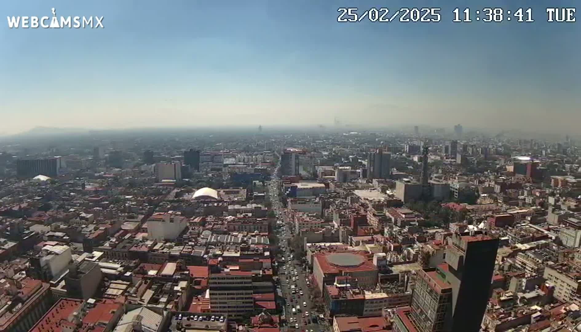 A hazy, sunny aerial view shows a sprawling city with numerous buildings and streets.