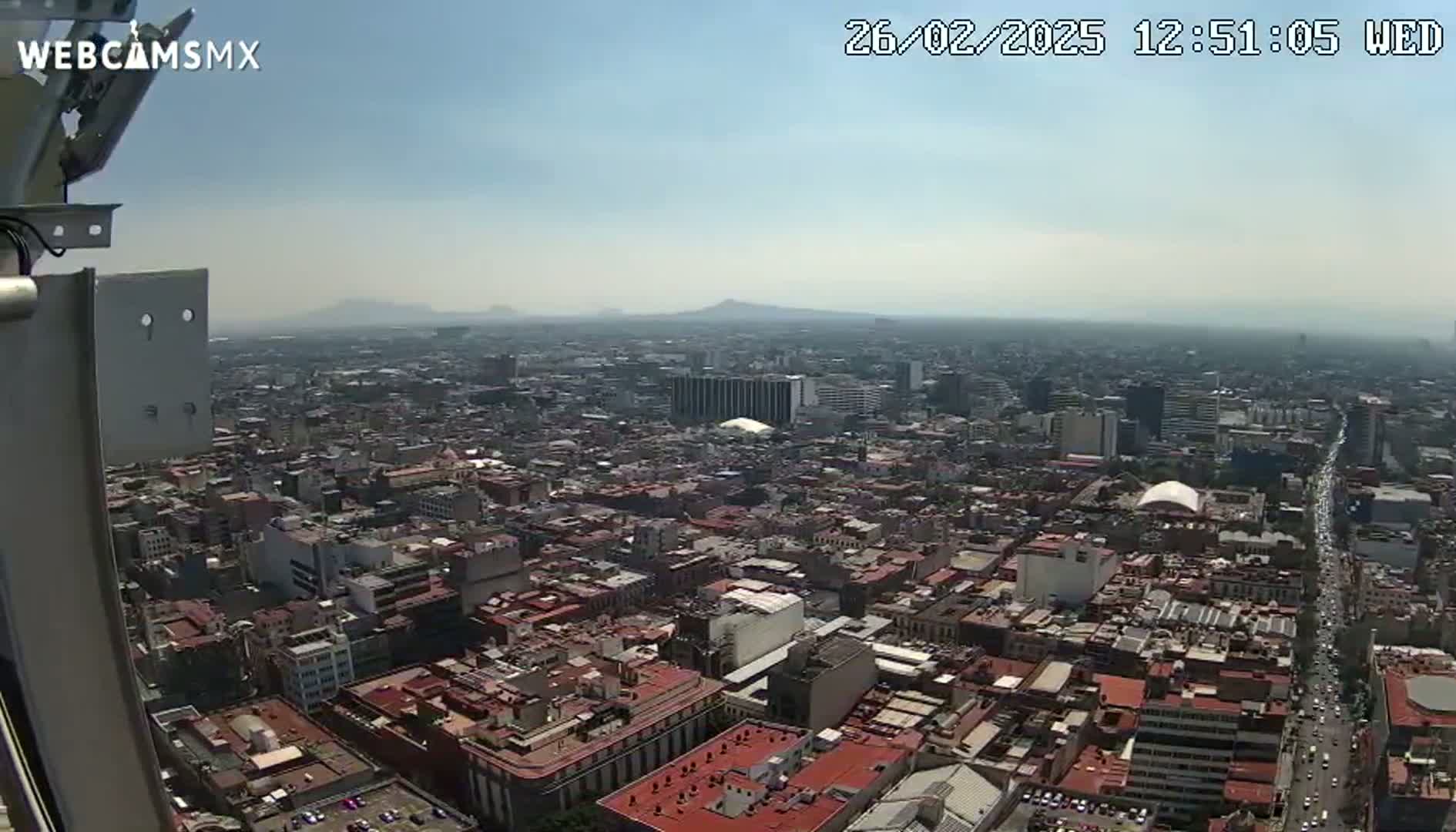 A hazy, sunny day reveals a sprawling cityscape extending to distant mountains.