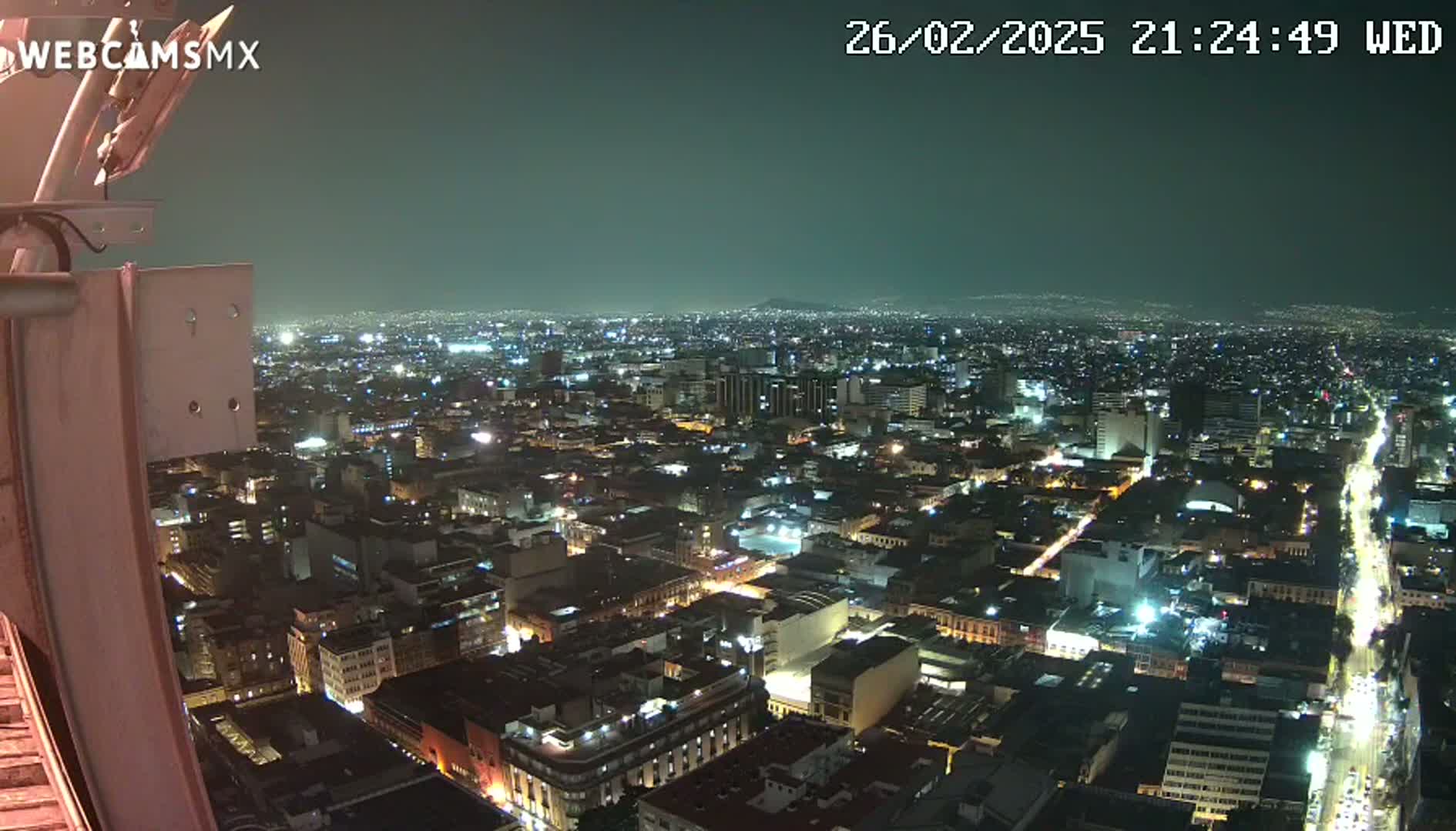 A nighttime, high-angle view shows a sprawling city illuminated by countless lights under a dark, clear sky.