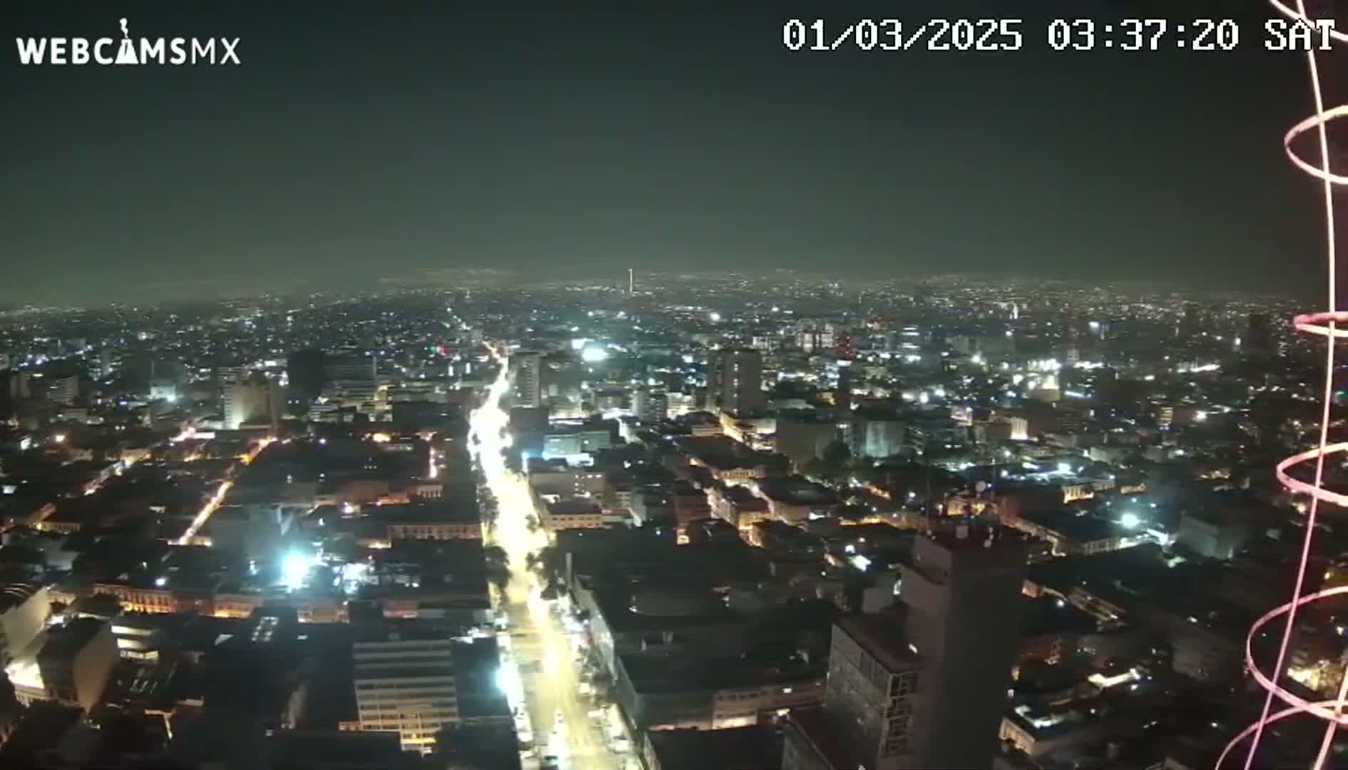 A nighttime, high-angle view of a sprawling city illuminated by streetlights and building lights under a hazy sky.