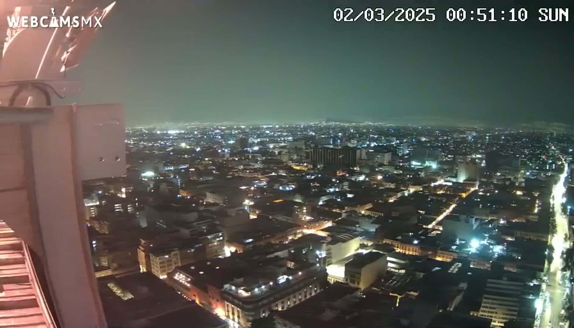 A nighttime view of a sprawling city illuminated by streetlights and building lights under a slightly hazy sky.