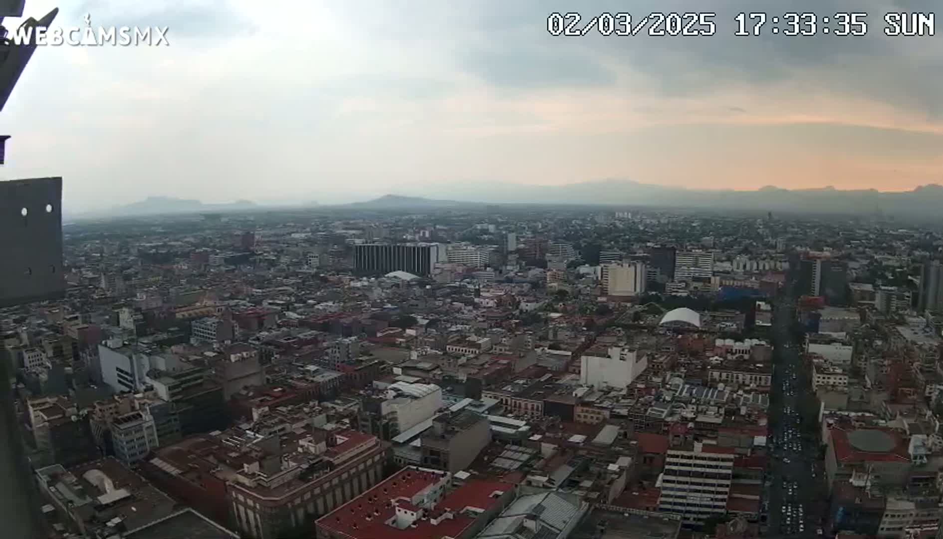 An expansive cityscape is viewed from a high vantage point under an overcast sky with a hint of sunset on the horizon.