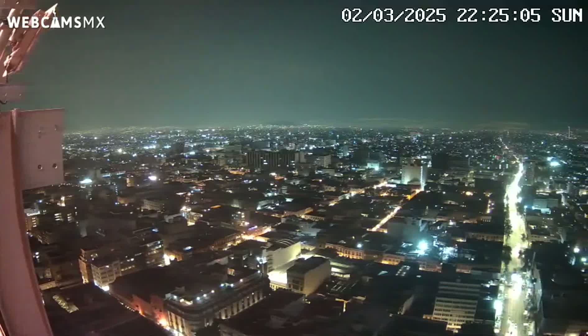 A nighttime, high-angle view of a sprawling city illuminated by numerous lights under a dark, clear sky.
