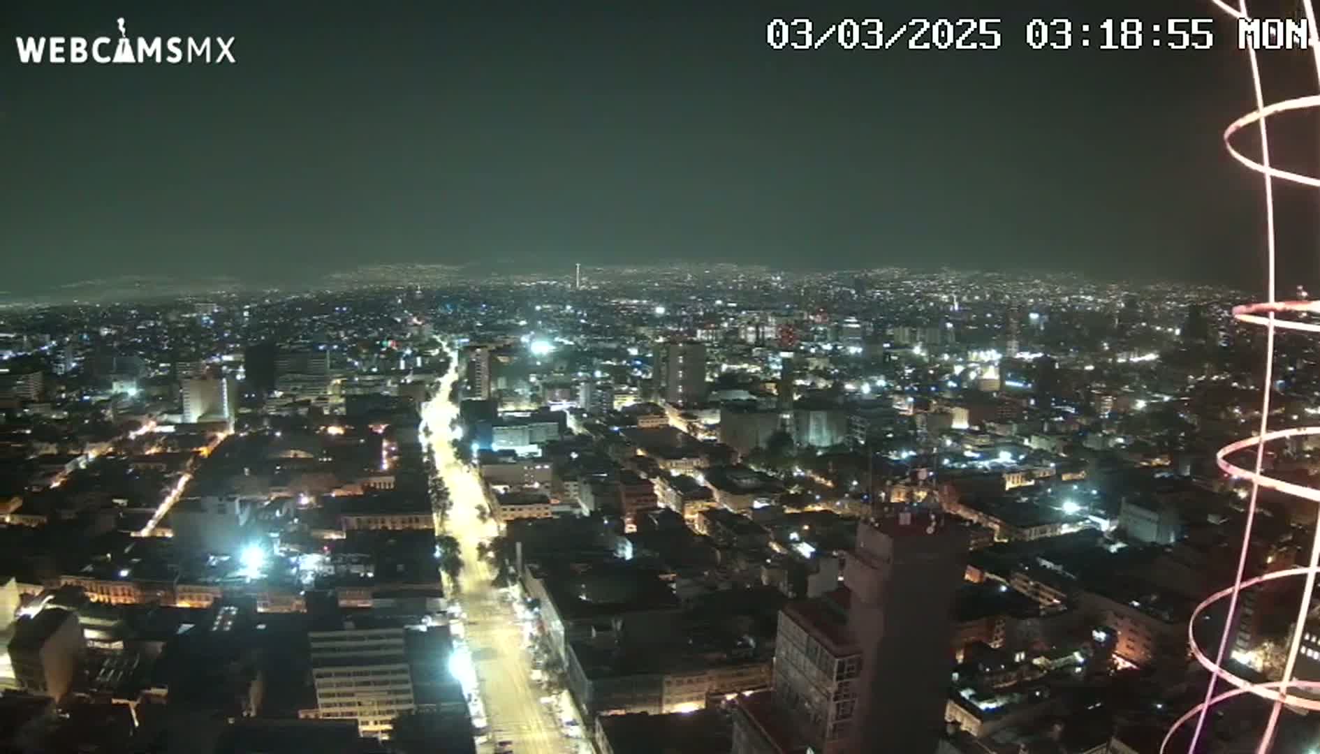 A nighttime, aerial view of a sprawling city illuminated by streetlights and building lights under a clear sky.