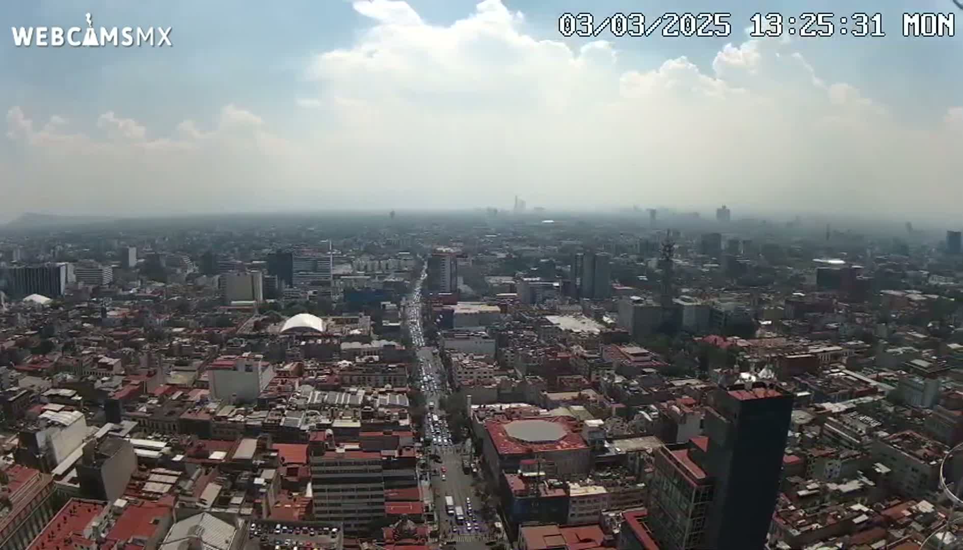A hazy, sunny day view of a vast cityscape, showing dense buildings and a long road with traffic.