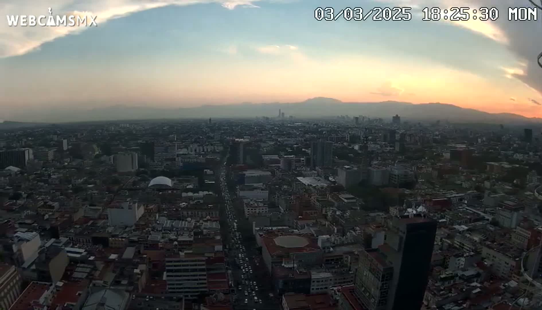 A high-angle, long shot of a sprawling city at sunset, under a mostly clear sky with a few clouds.