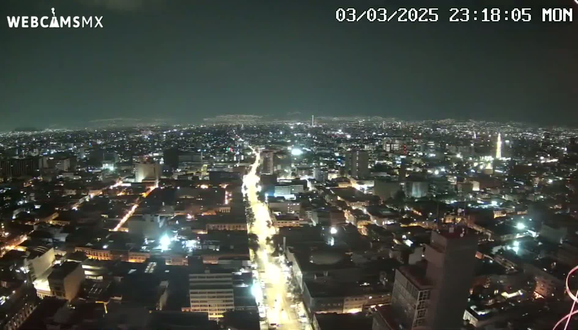 A nighttime aerial view of a sprawling city illuminated by streetlights and building lights under a clear sky.