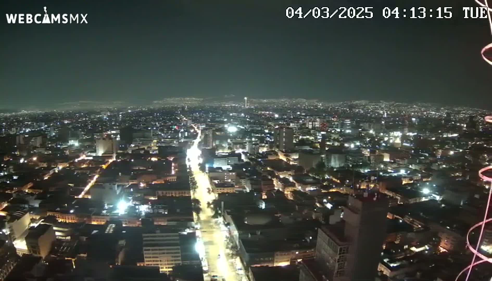 A nighttime aerial view shows a sprawling city illuminated by streetlights and building lights under a clear, dark sky.