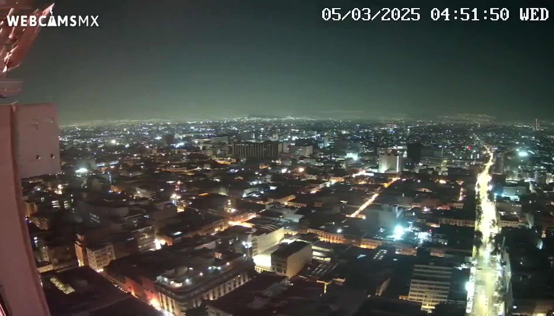 A nighttime, high-angle view of a sprawling city illuminated by streetlights and building lights under a dark sky.