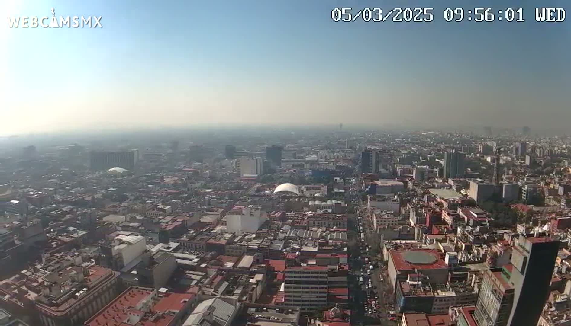 A hazy, sunny day reveals a sprawling cityscape of dense, low-rise buildings extending to the horizon.