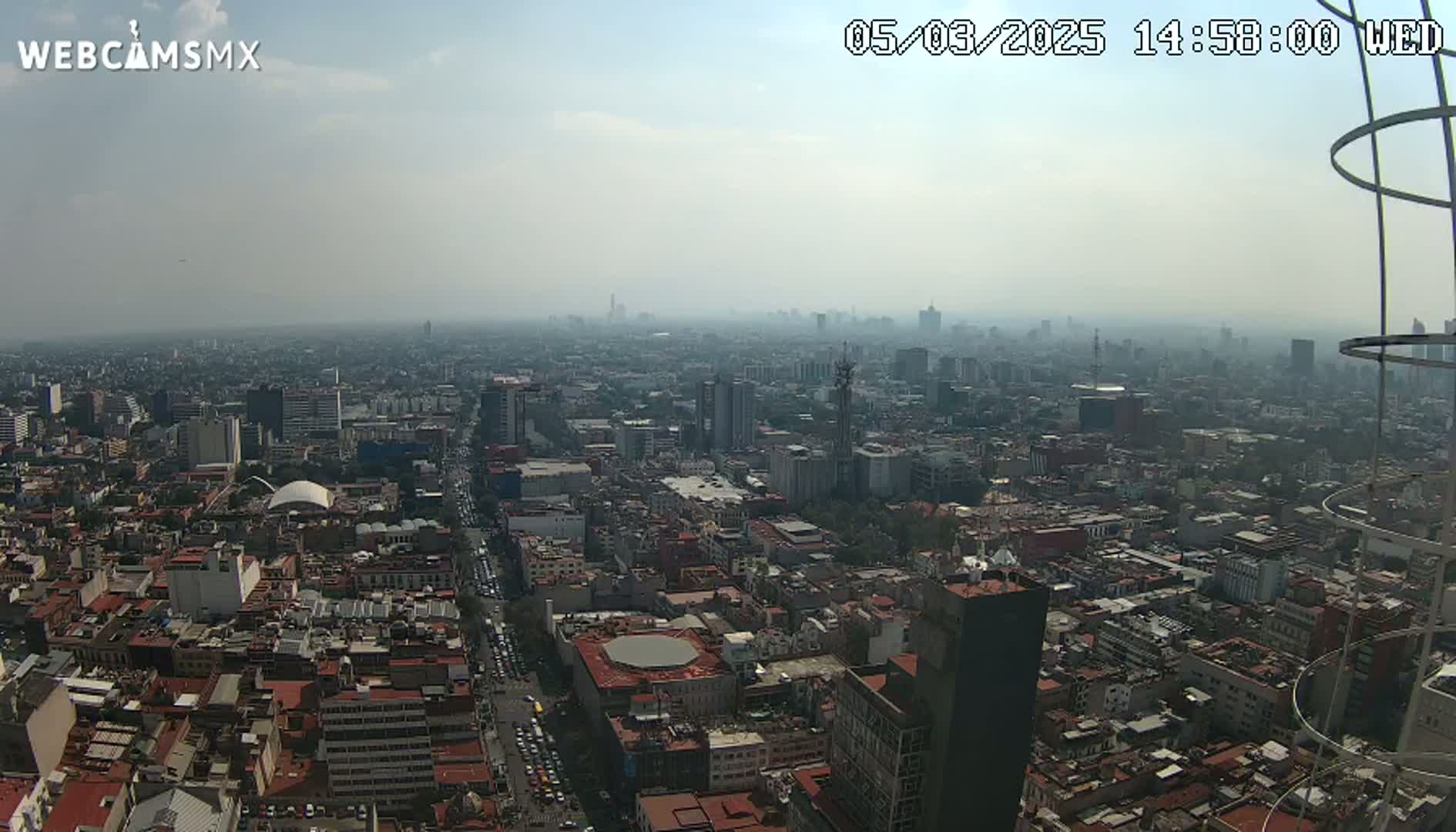 A hazy, high-angle view shows a sprawling city with numerous buildings under a partly cloudy sky.