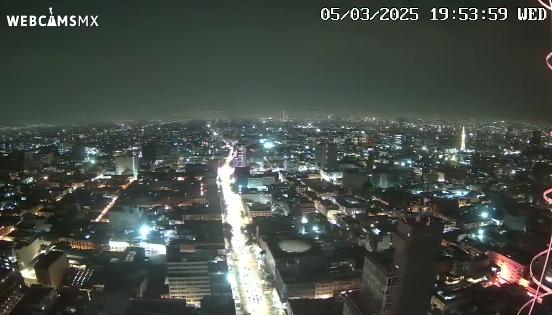 A nighttime, high-angle view of a sprawling city with brightly lit streets and buildings under a hazy, dark sky.