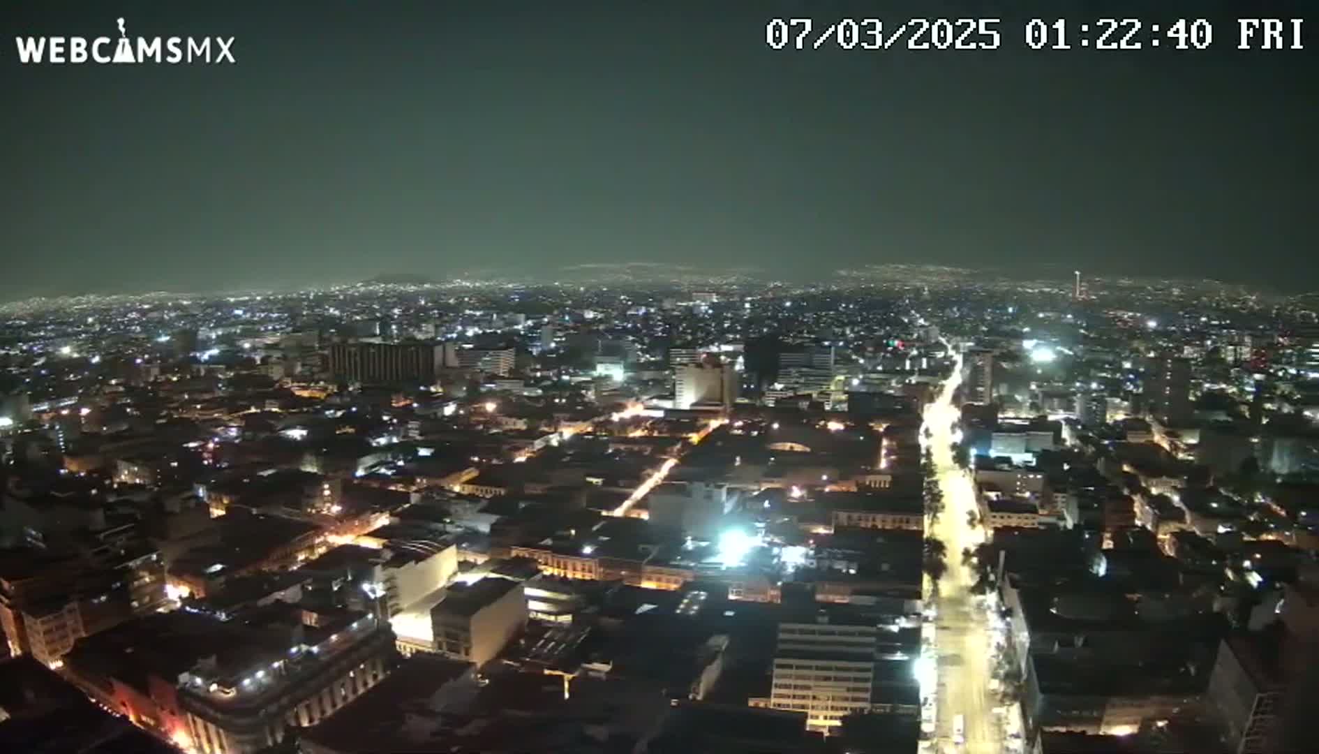A nighttime aerial view of a sprawling city with illuminated streets and buildings under a dark, clear sky.