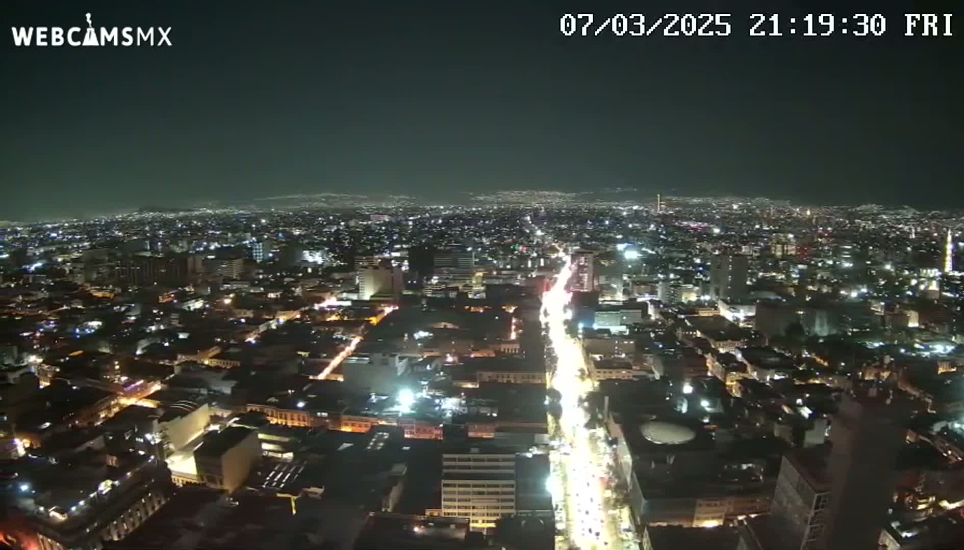 A nighttime aerial view shows a sprawling city with brightly lit streets and buildings under a clear sky.