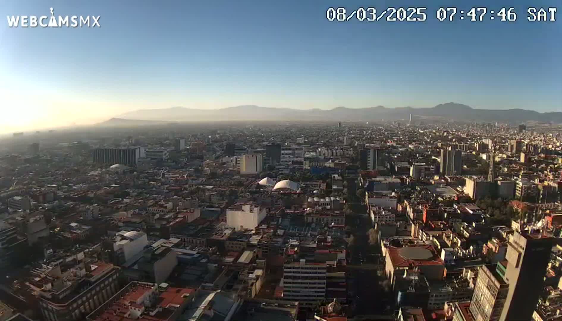 A hazy, sunny morning view of a sprawling city with distant mountains.