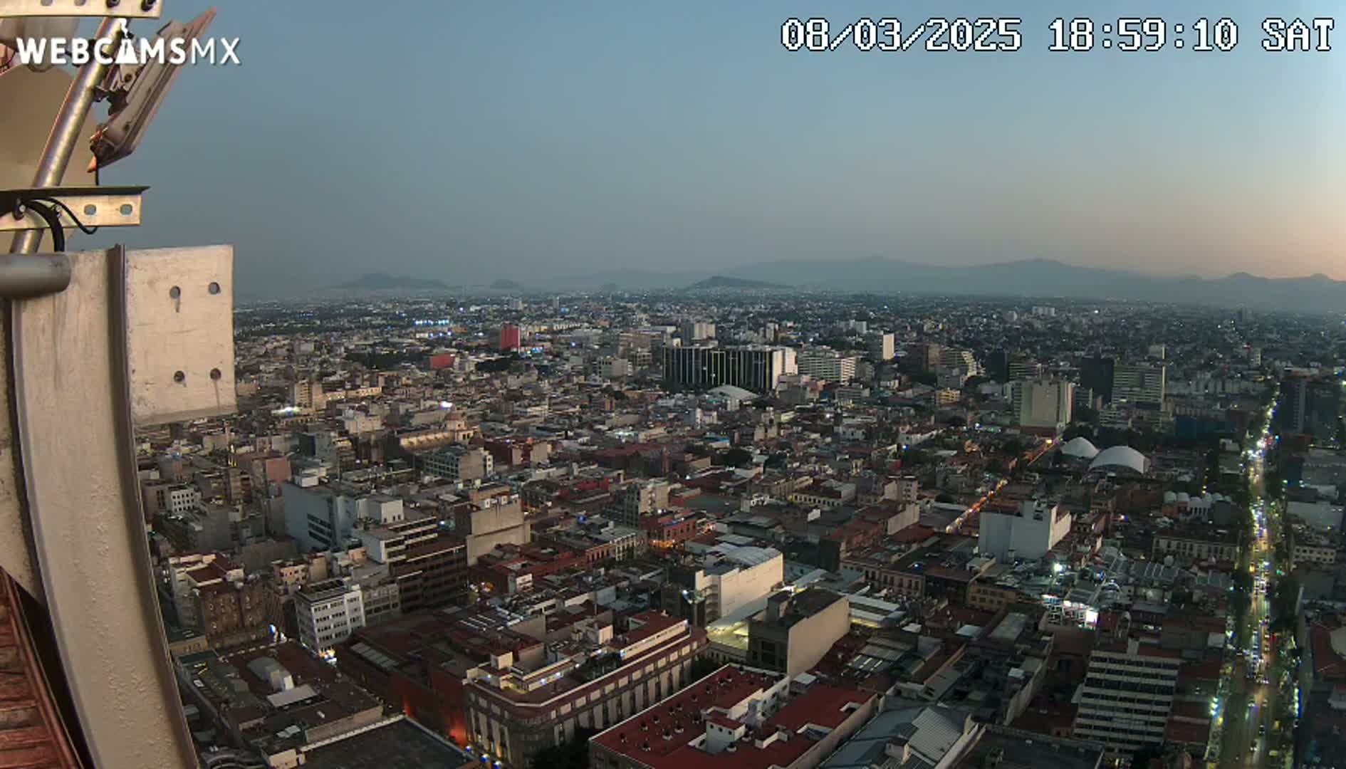 A high-angle, twilight view of a sprawling city with distant mountains under a clear sky.