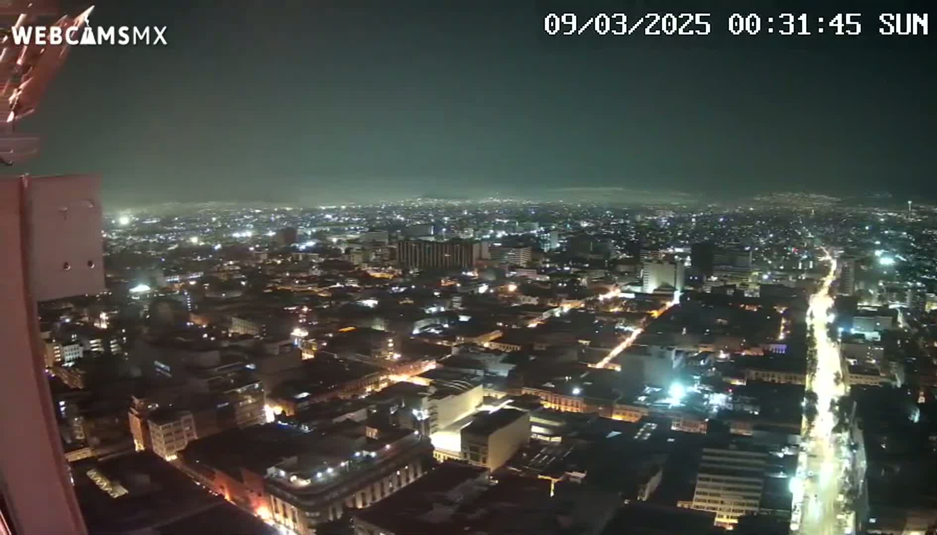 A nighttime, high-angle view of a sprawling city with illuminated streets and buildings under a dark sky.