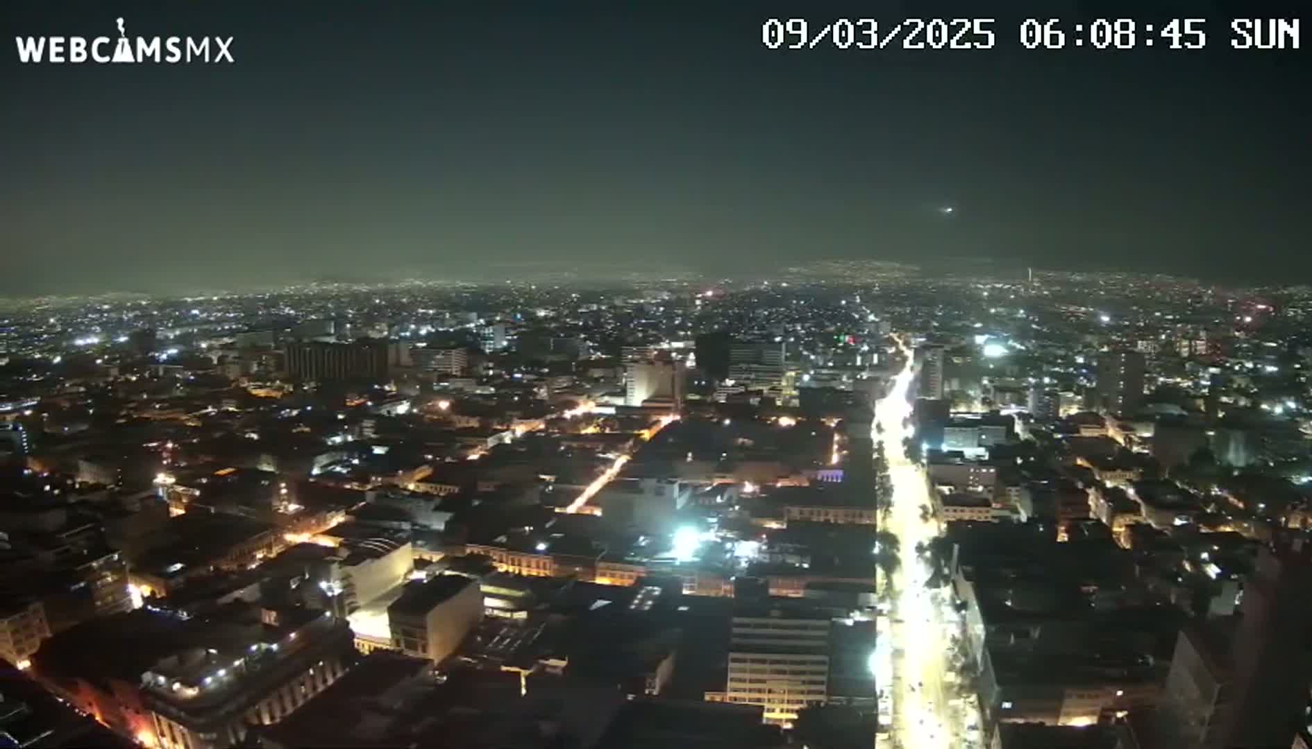 A nighttime aerial view of a densely populated city with brightly lit streets and buildings under a clear sky.