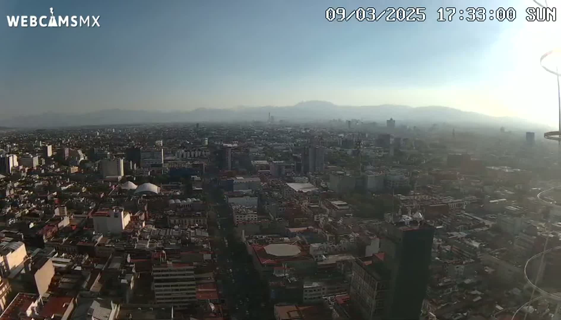 A hazy, sunny day reveals a sprawling cityscape extending to distant mountains.