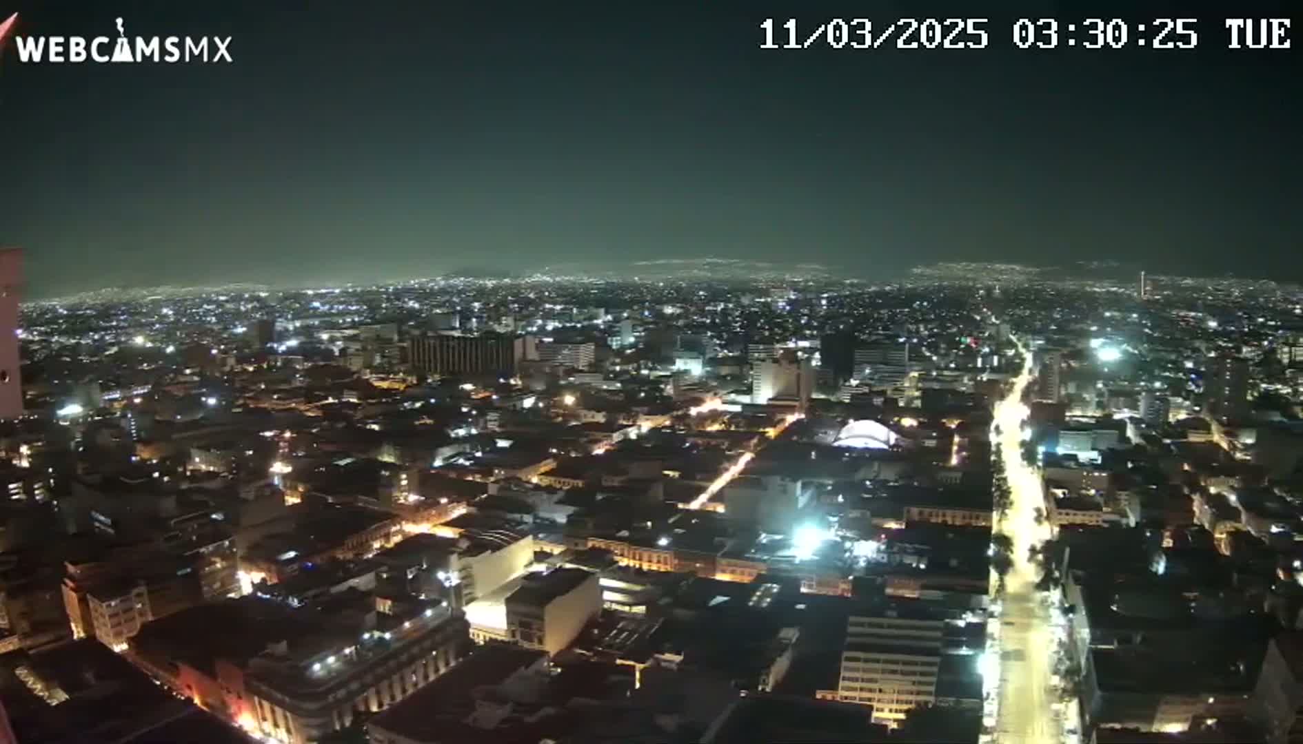 A nighttime aerial view of a sprawling city with illuminated streets and buildings under a clear, dark sky.