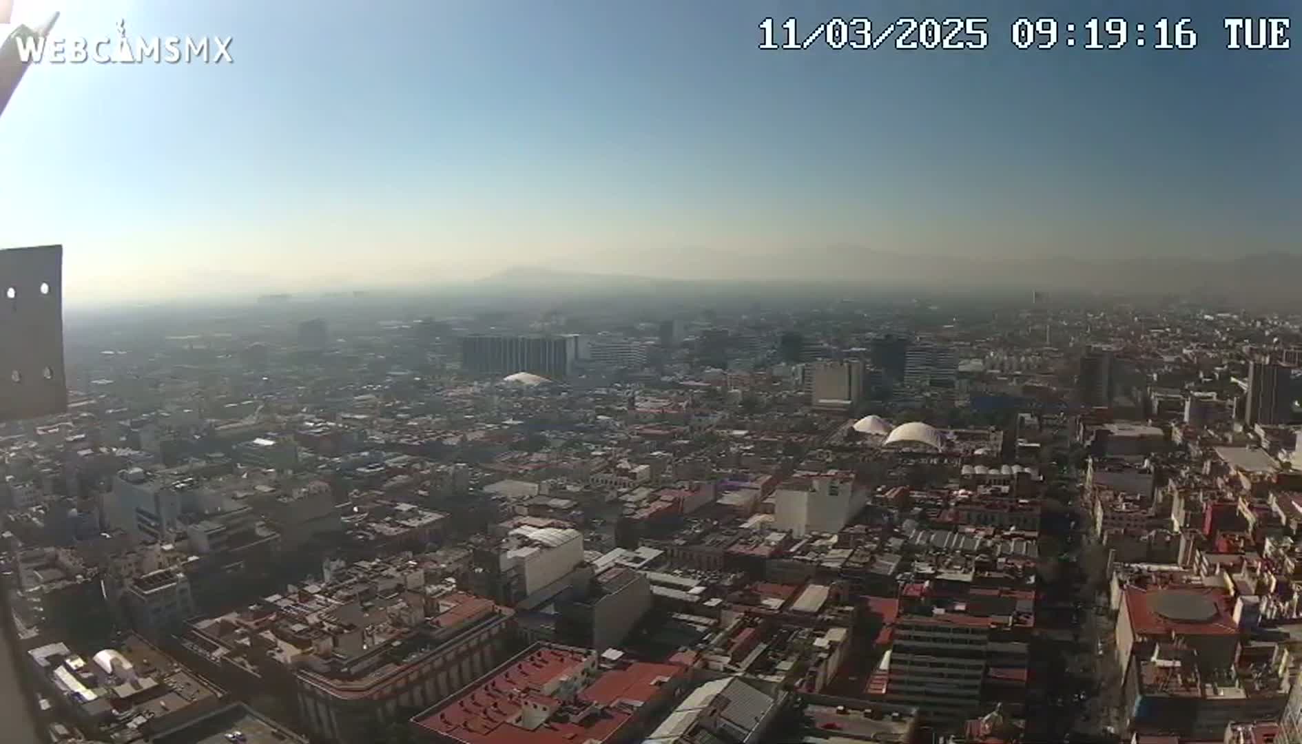 A hazy, sunny day reveals a sprawling cityscape viewed from a high vantage point.