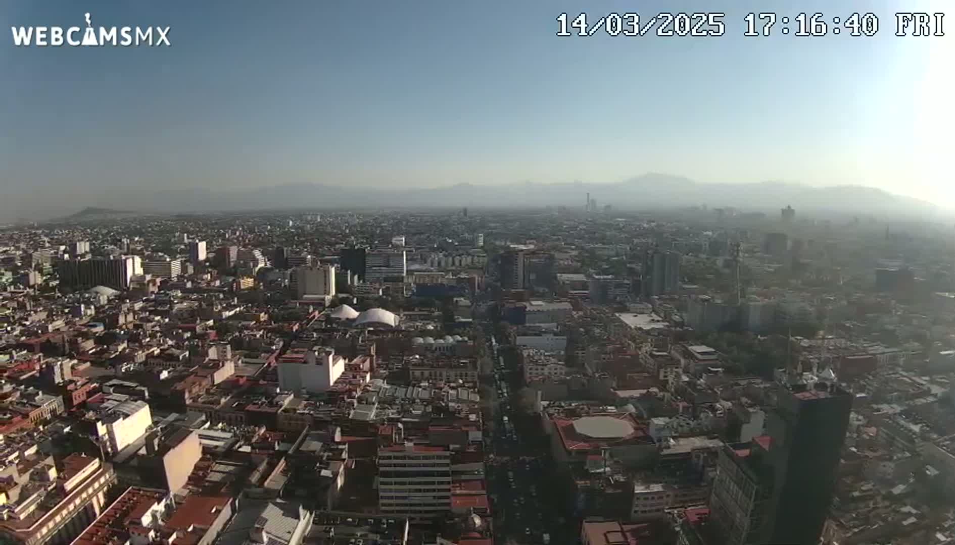 A hazy, sunny aerial view of a sprawling city with distant mountains in the background.