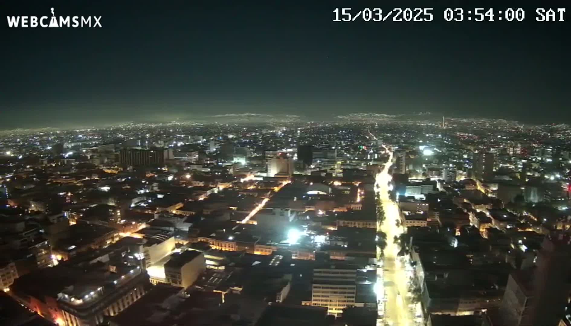 A nighttime aerial view of a sprawling city with brightly lit streets and buildings under a clear, dark sky.