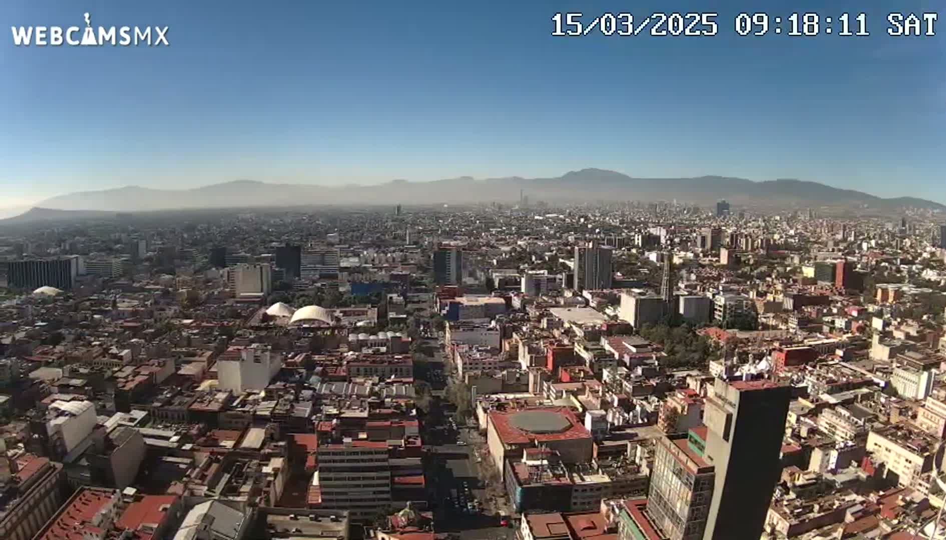 A hazy, sunny day reveals a sprawling cityscape with distant mountains under a clear blue sky.