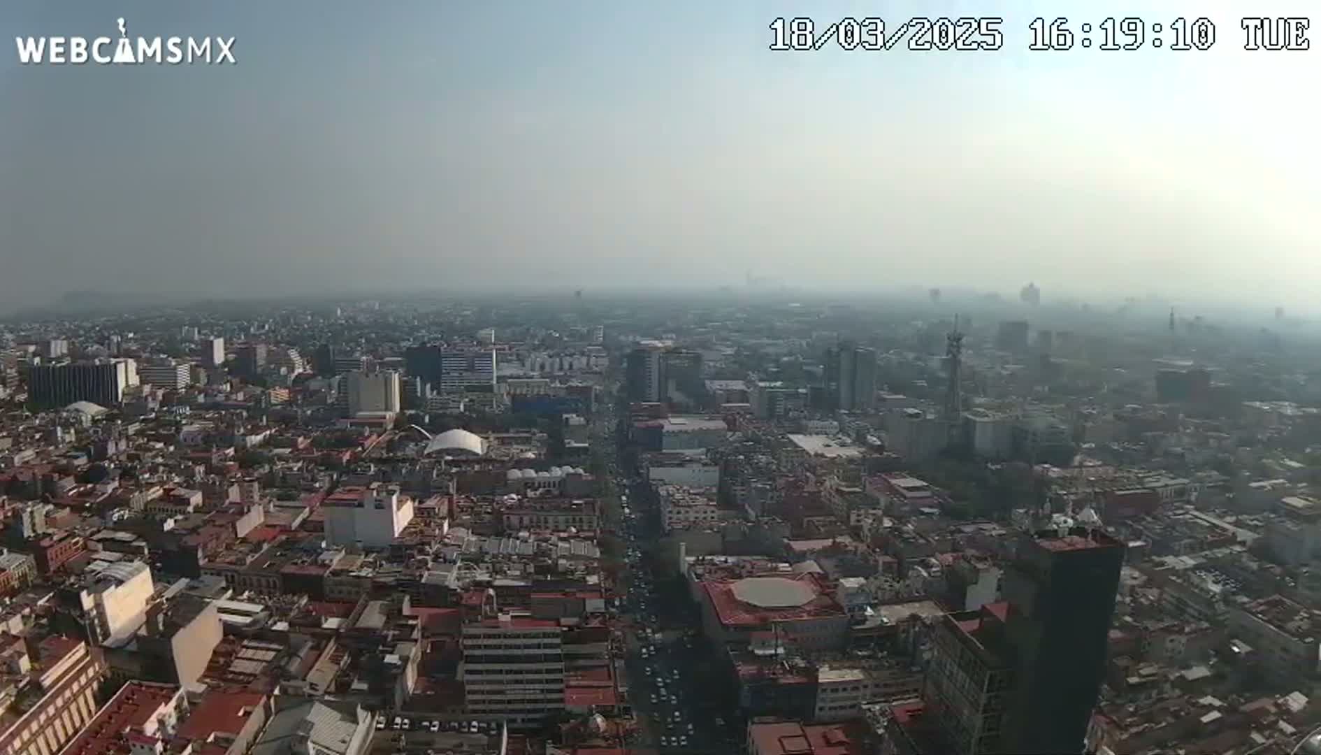 A hazy, high-angle view of a sprawling city with numerous buildings and streets extending to the horizon.