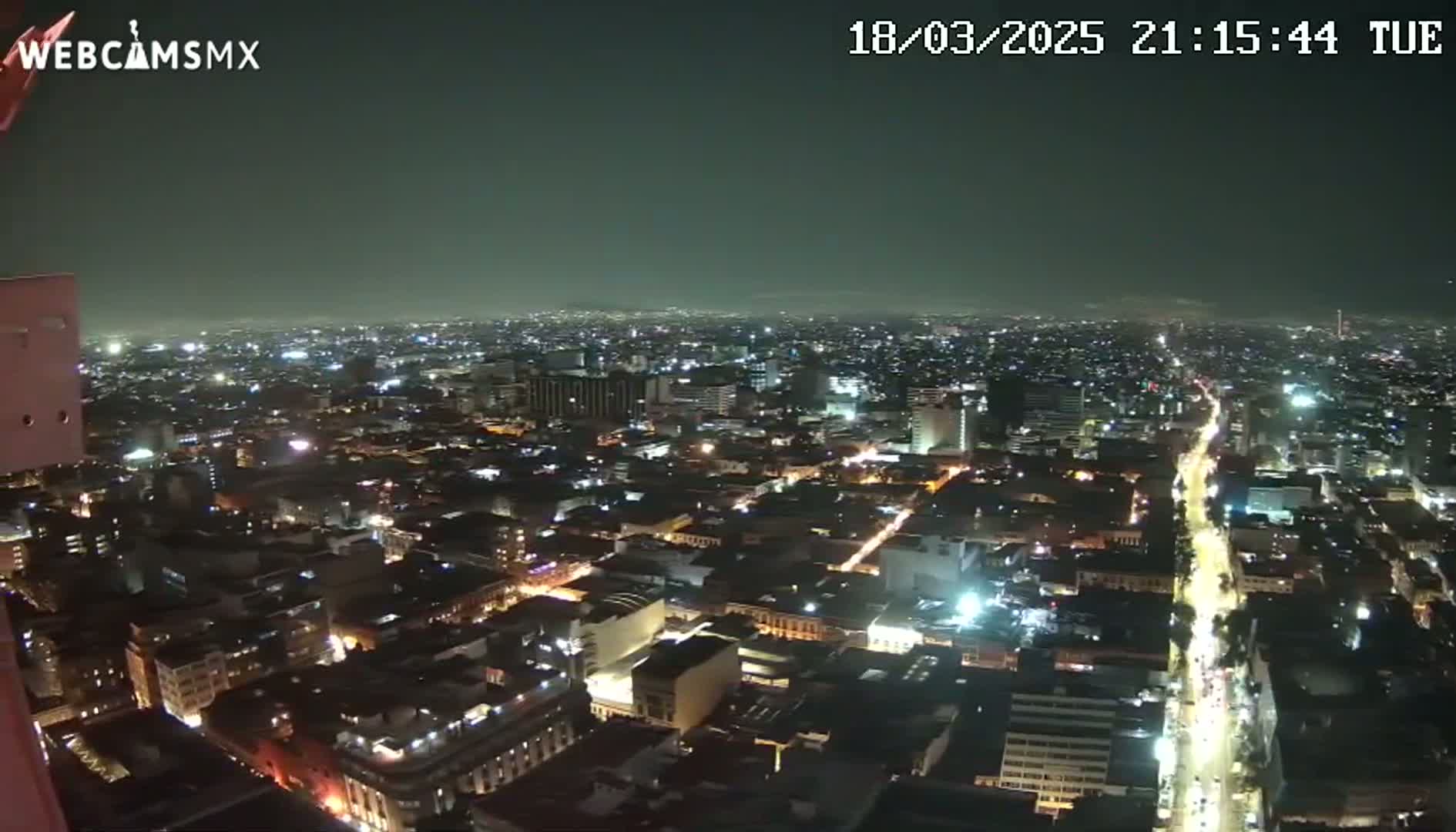 A nighttime, high-angle view shows a sprawling city illuminated by numerous lights under a dark sky.