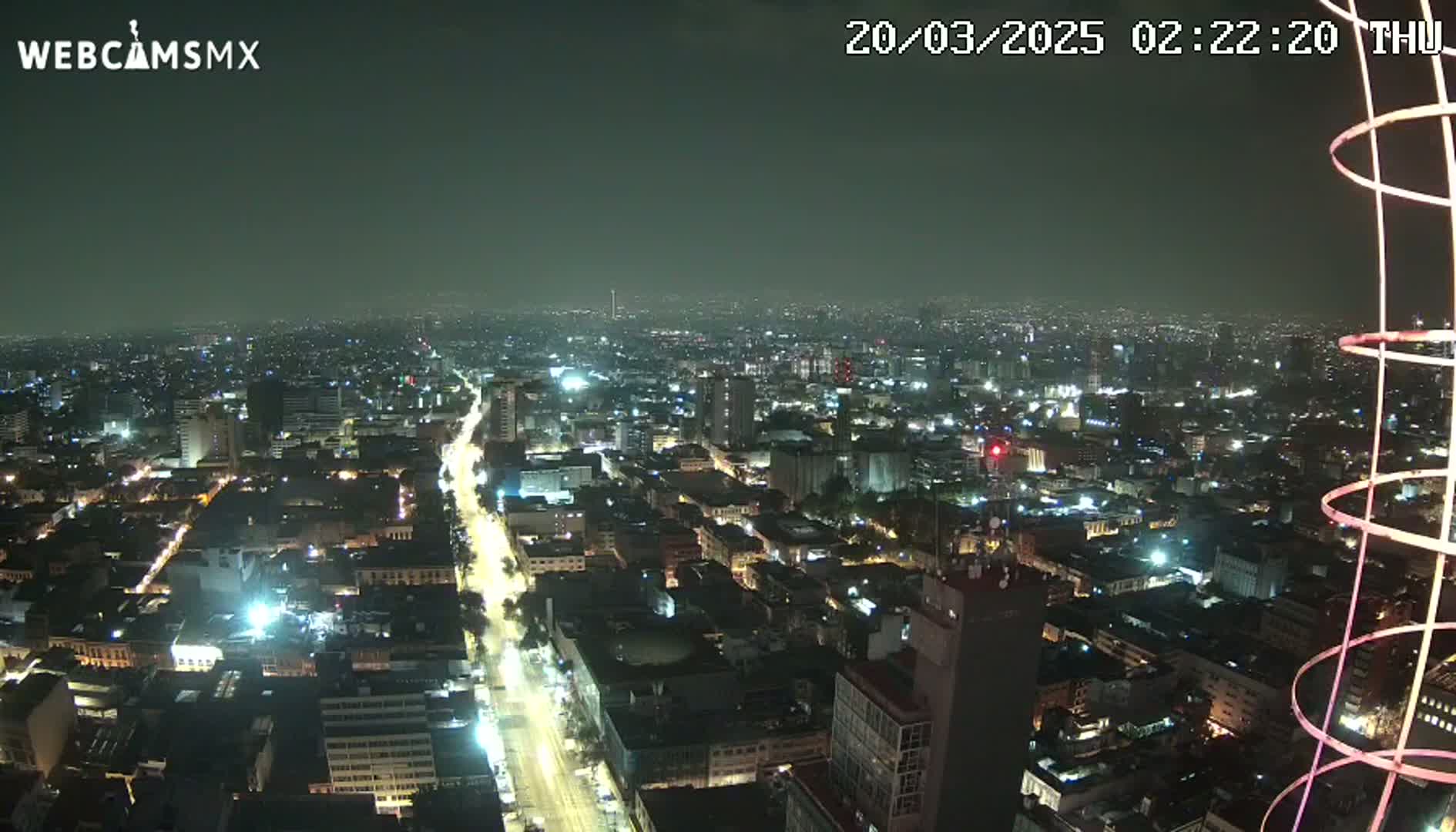 A nighttime, high-angle view of a brightly lit city sprawling across a vast area under a hazy sky.