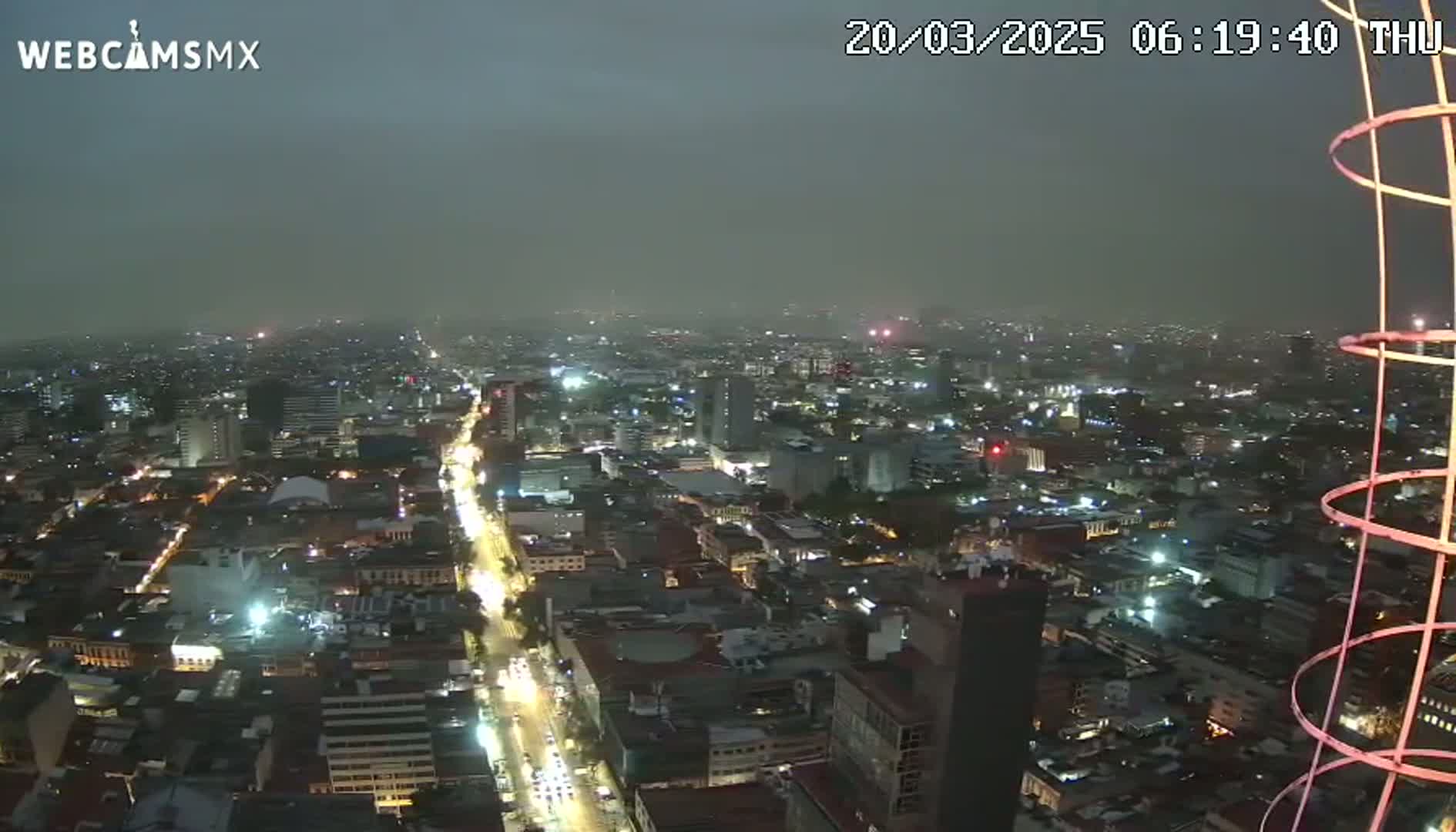 A nighttime aerial view of a city under hazy, overcast conditions shows brightly lit streets and buildings.