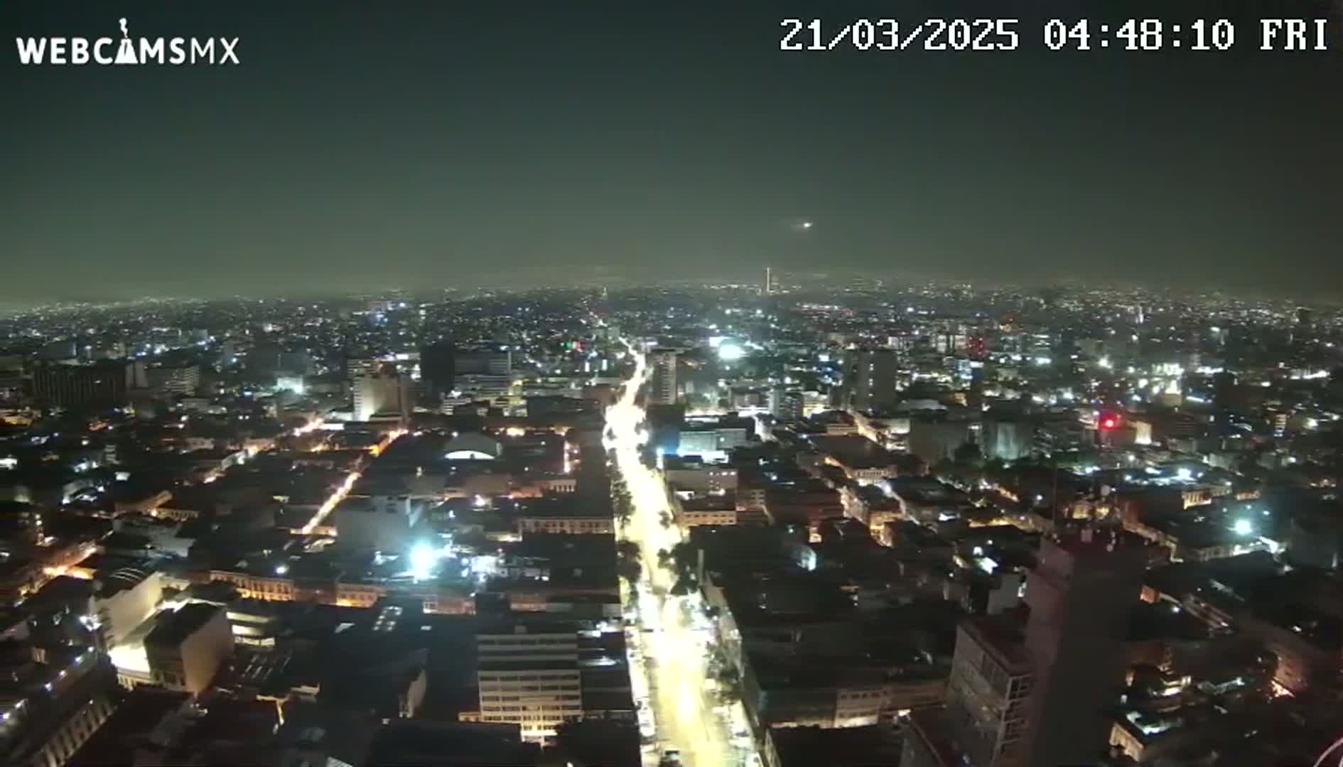 A nighttime, hazy aerial view of a sprawling city with brightly lit streets and buildings.