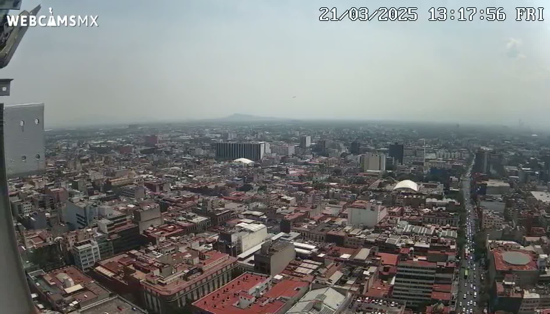 A hazy, high-angle view of a sprawling city, showing densely packed buildings and streets with cars, under a light gray sky.