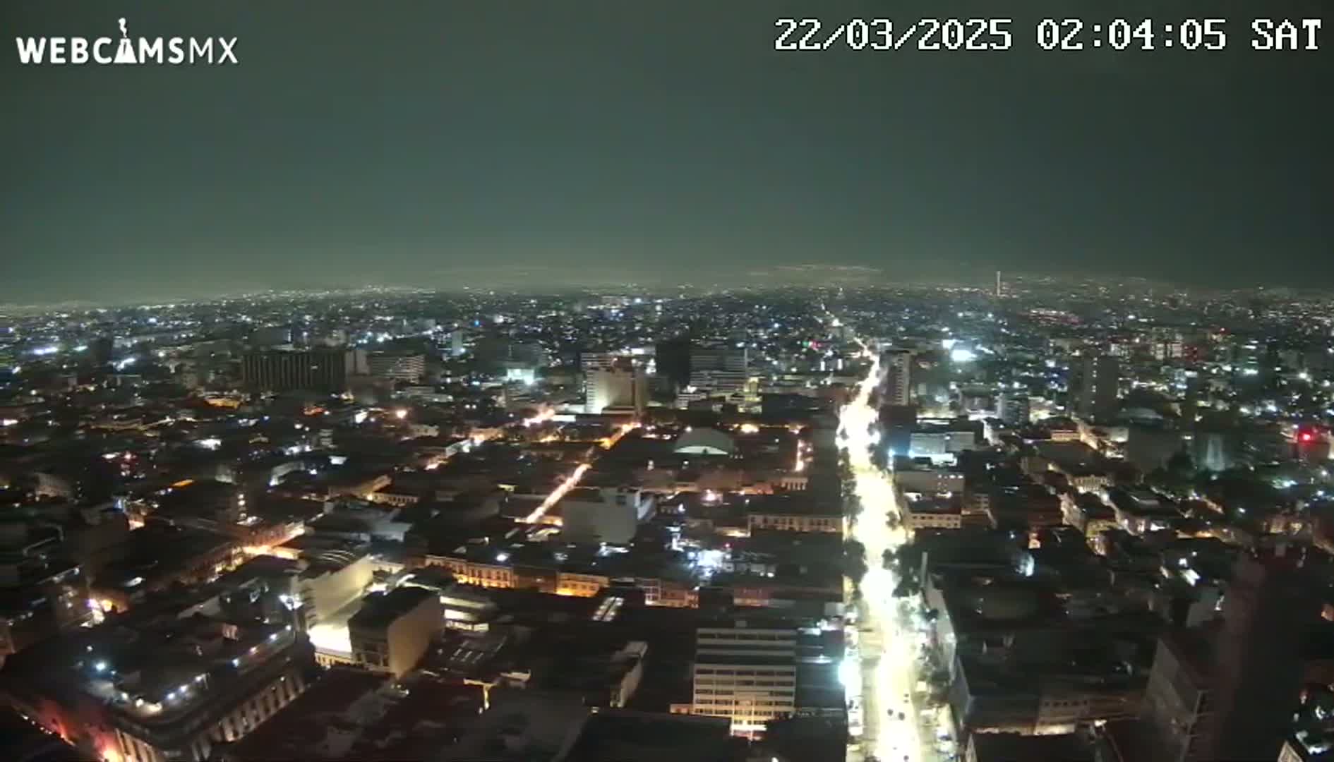 A nighttime aerial view of a city with a long, brightly lit street running through it under a clear, dark sky.