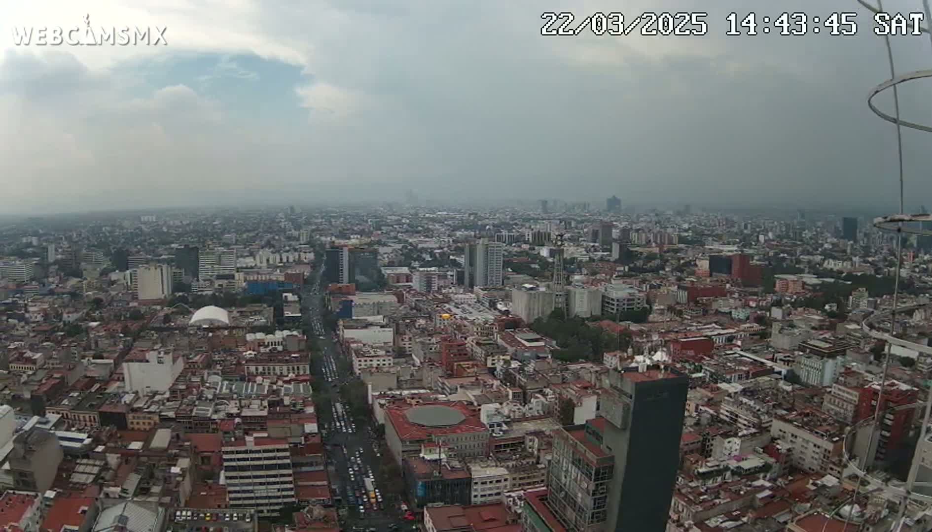 An expansive aerial view of a sprawling city under a cloudy sky shows many buildings and streets.