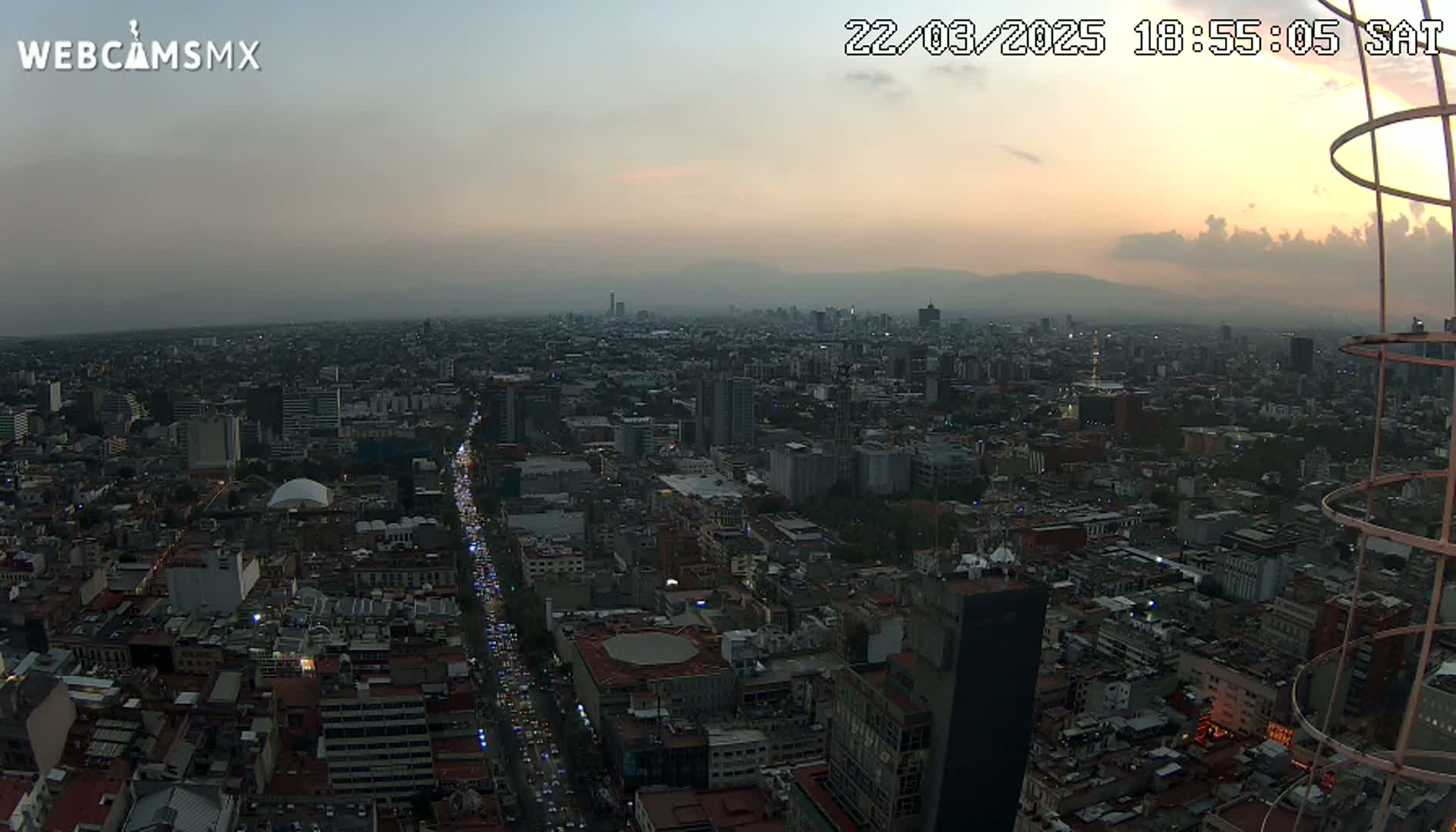 An aerial view at dusk shows a sprawling city with a busy street below, under a hazy sky.