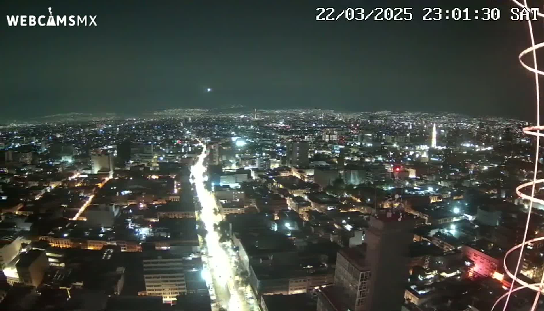 A nighttime, high-angle view of a sprawling city with brightly lit streets and buildings under a clear, dark sky.