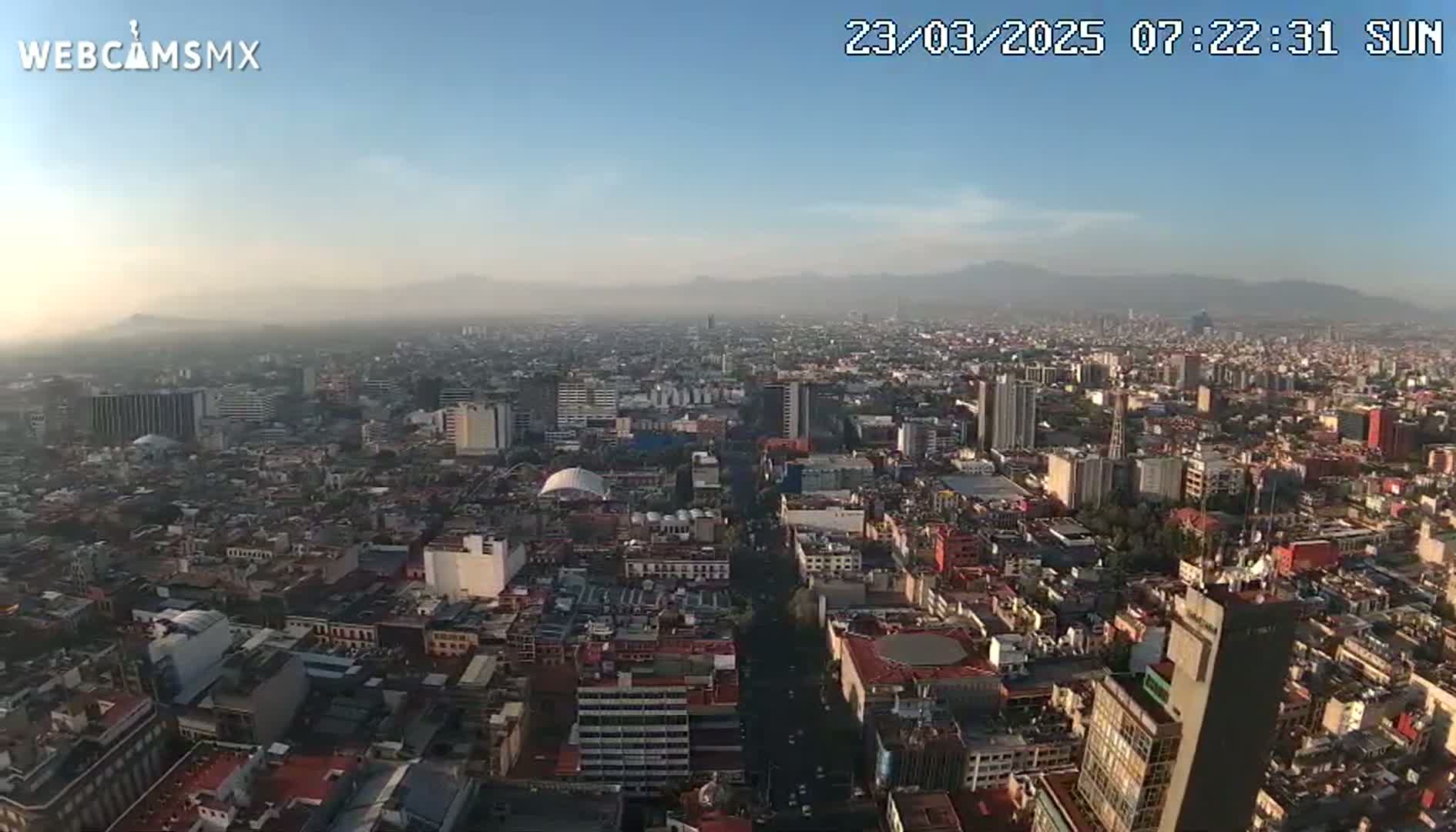 A hazy, sunny day overlooks a sprawling cityscape with distant mountains under a clear sky.