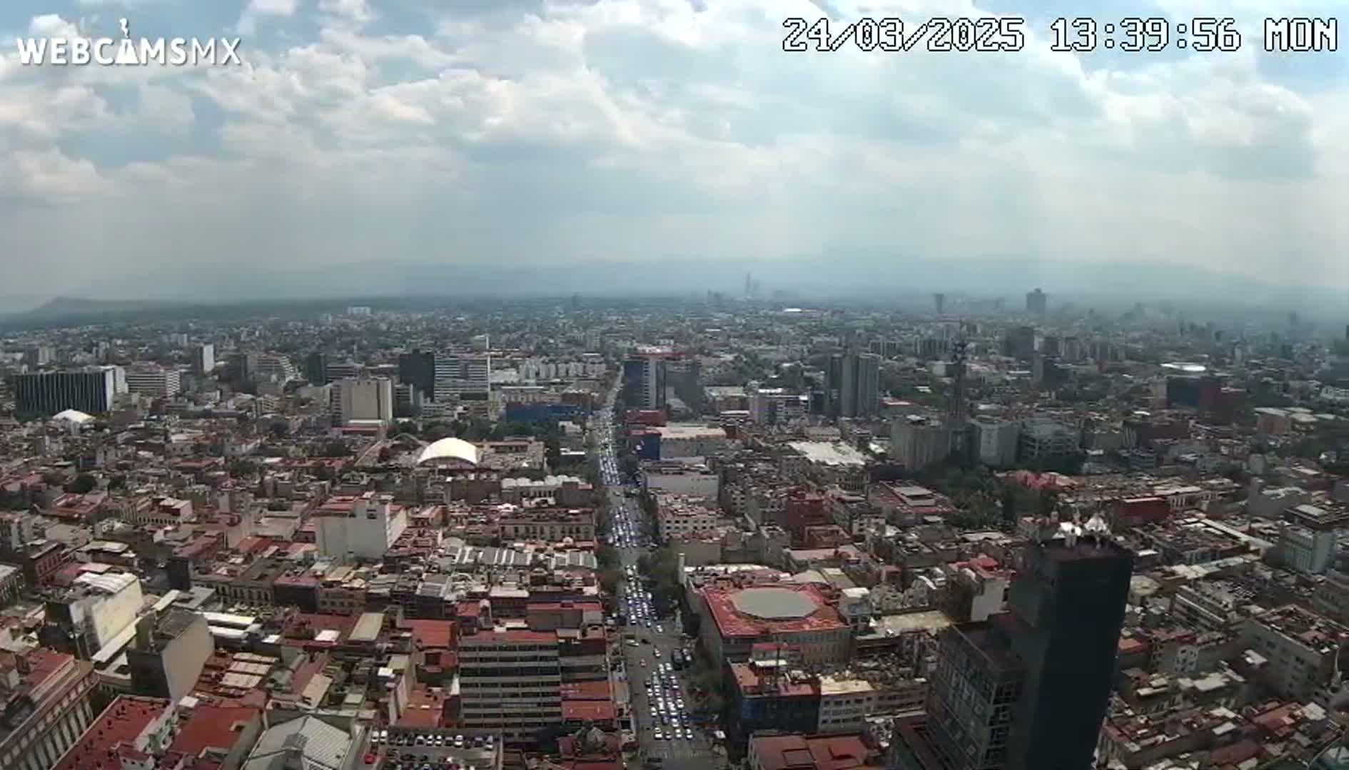 A partly cloudy day reveals a sprawling cityscape with numerous buildings and a long avenue filled with vehicles.