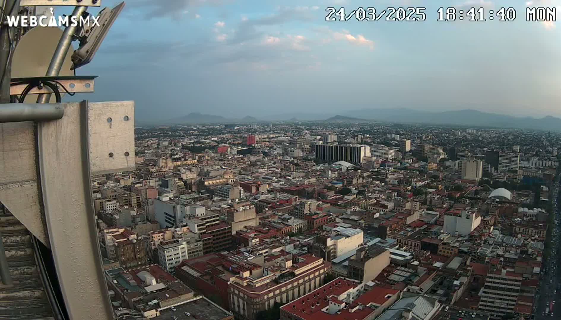 A high-angle, twilight view of a sprawling city with distant mountains under a partly cloudy sky.
