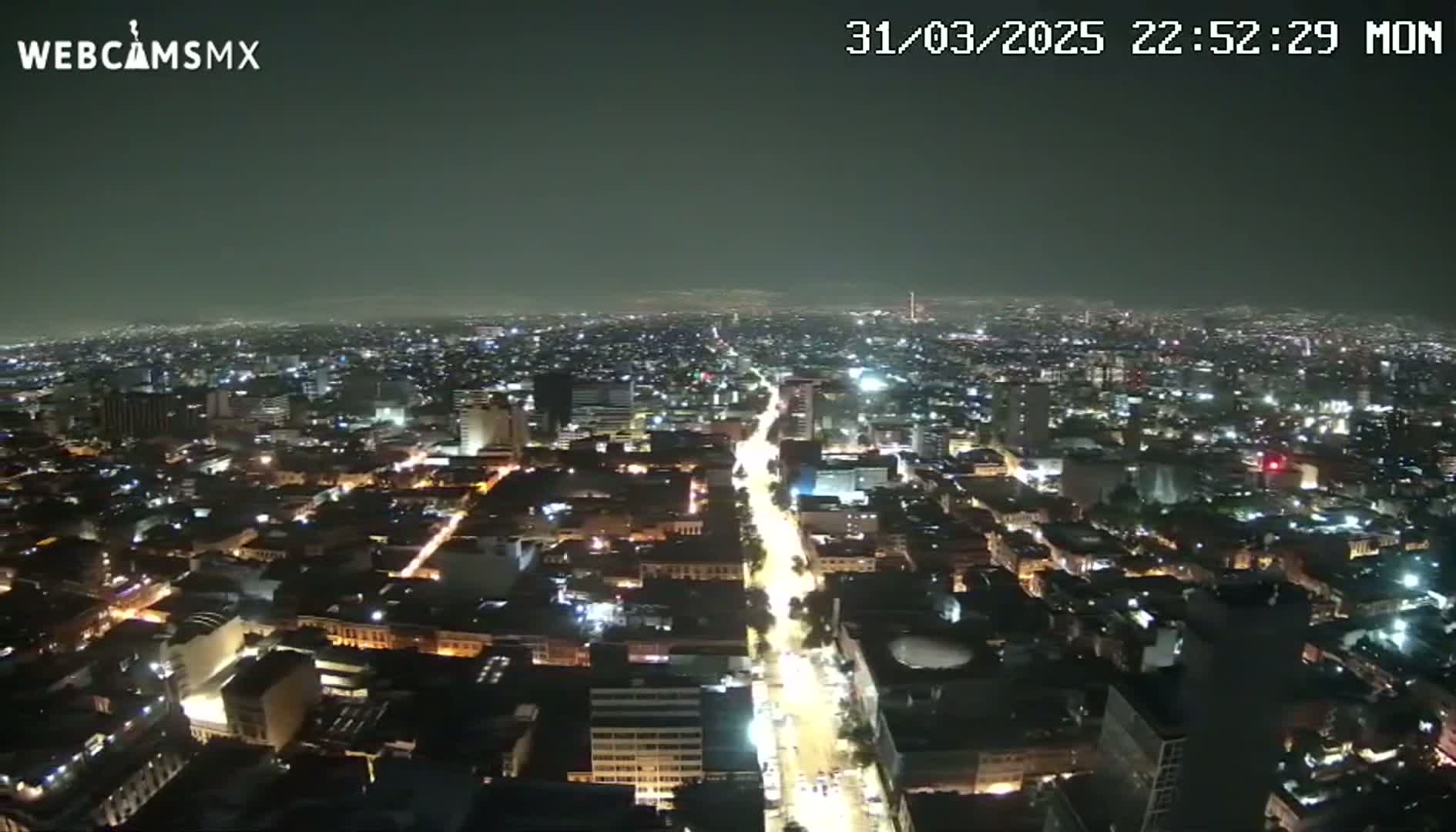 A nighttime, aerial view of a sprawling city with illuminated streets and buildings under a dark, clear sky.