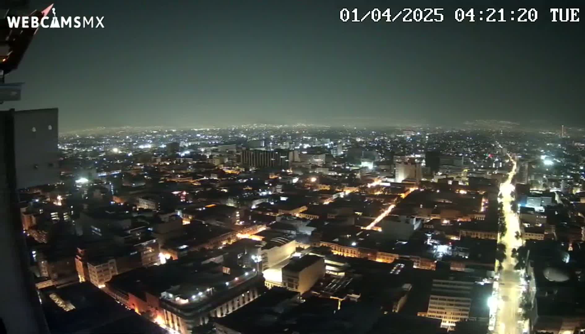 A nighttime, aerial view of a sprawling city with dimly lit streets and buildings under a hazy sky.